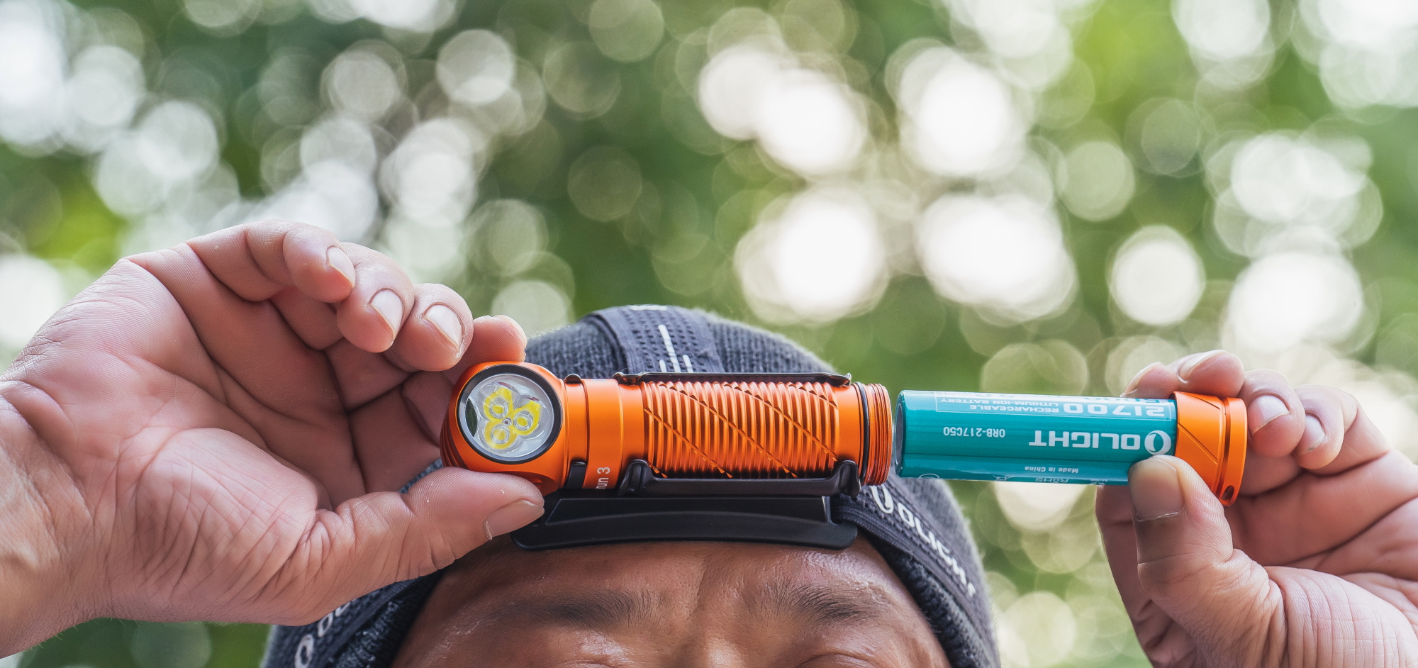 Olight Perun 3ヘッドランプに21700充電式バッテリーを装着する男性。アウトドア活動に最適な明るいヘッドライト。