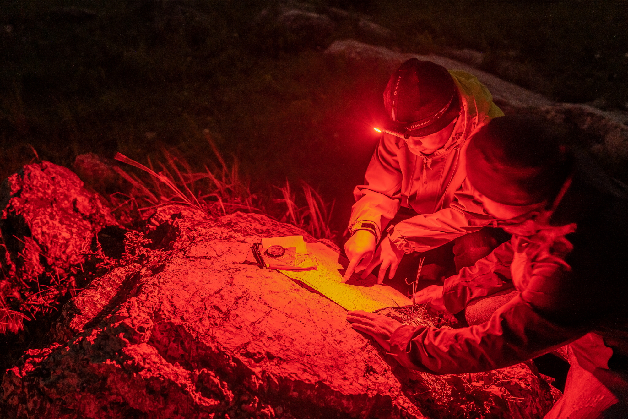 夜間、赤いヘッドライトの明かりで地図を確認する二人の登山者