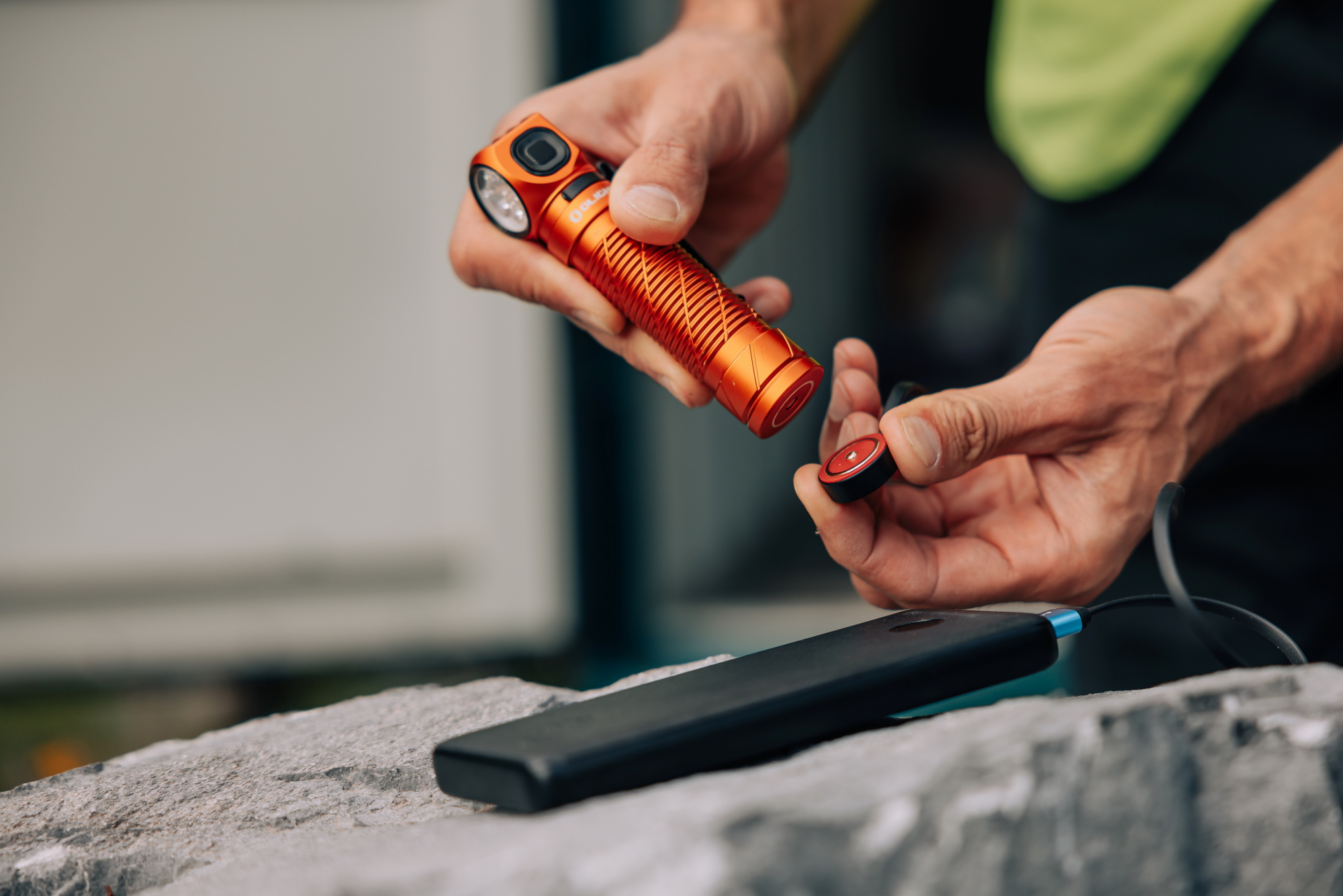 Orange Olight flashlight being charged with a magnetic charger connected to a power bank.