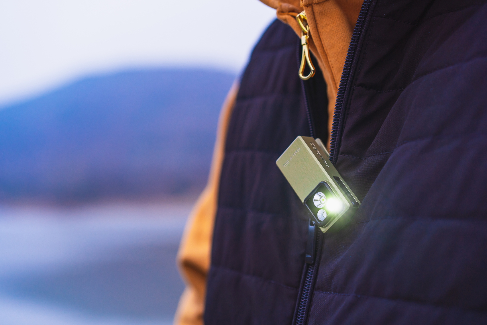 Olive green compact clip-on flashlight attached to a black shirt collar