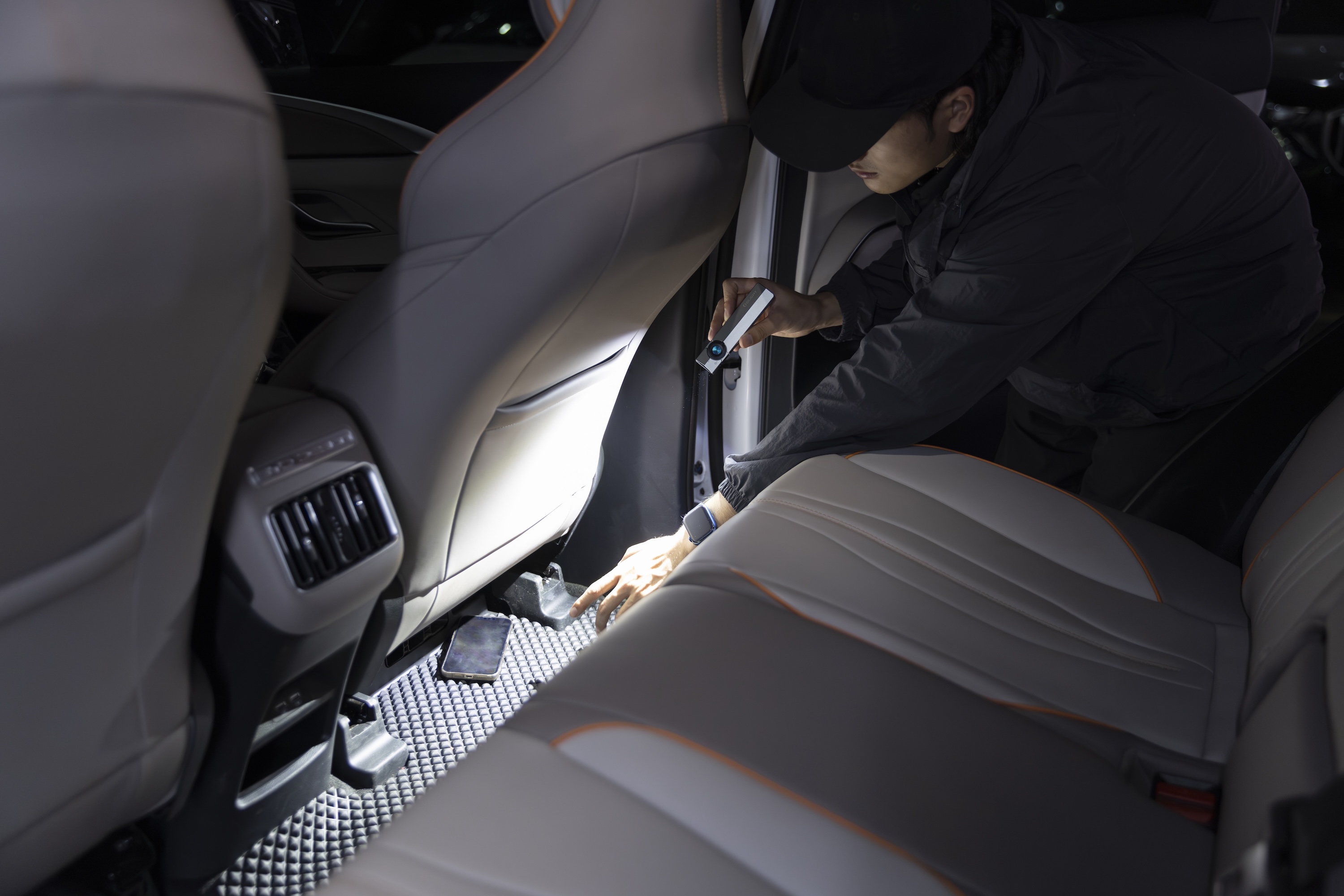 Man using a portable LED flashlight to find a lost phone on a car floor mat at night. Bright EDC pocket light for searching car interiors and emergency lighting.
