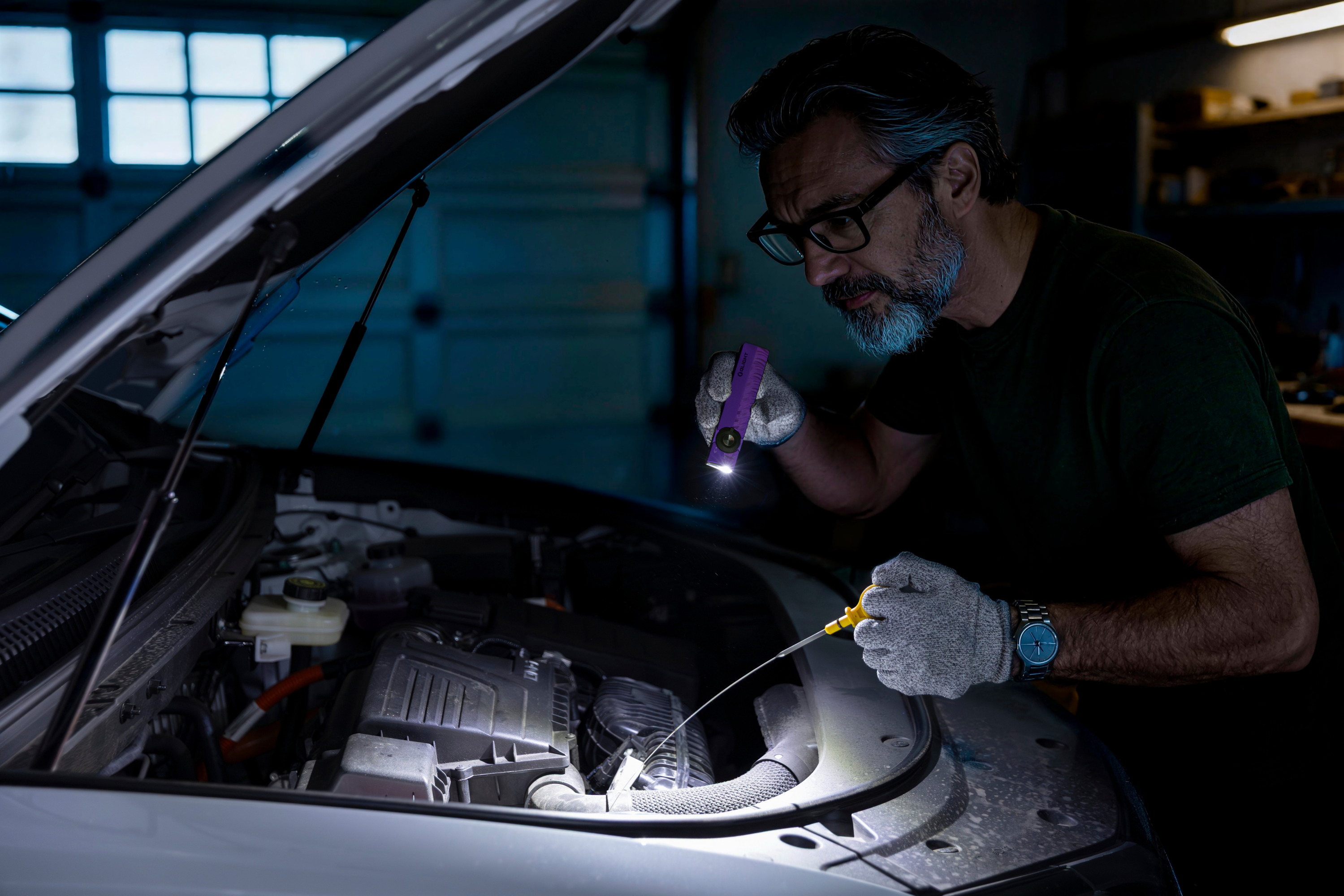 Olight ArkPro flashlight magnetically attached to a car's steel hood frame, lighting up the vehicle engine bay for convenient hands-free inspection and repair.