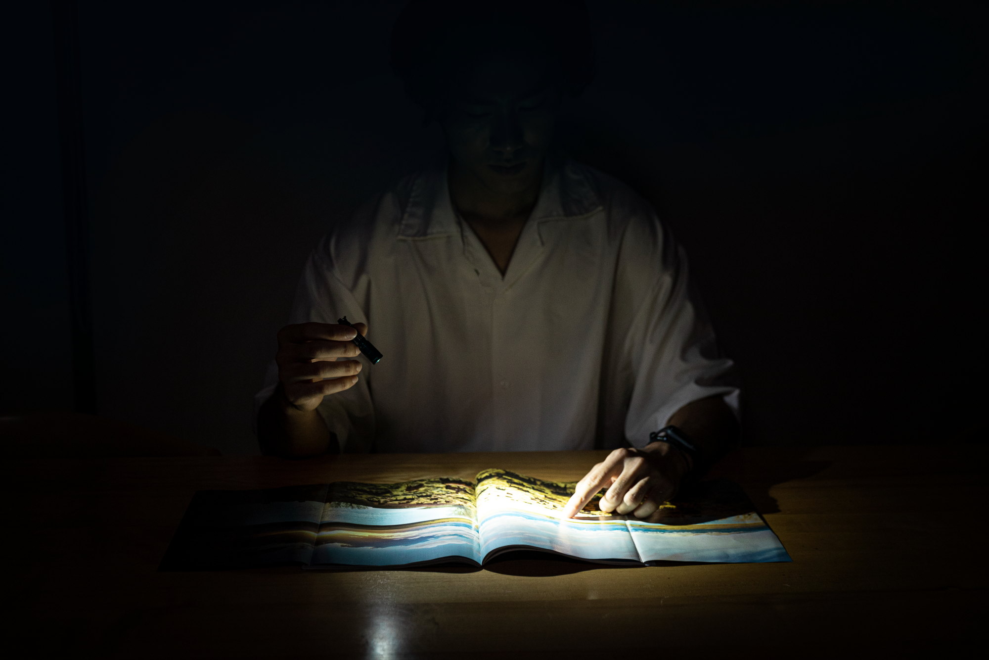 Man using a small LED flashlight to read a map in a dark room