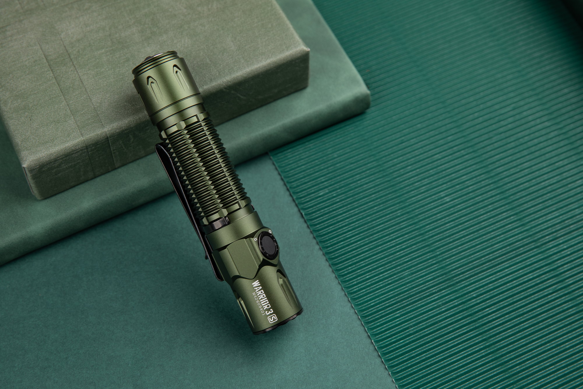 Lampe torche tactique Olight Warrior 3S verte sur fond texturé, idéale pour l'aventure et l'extérieur.