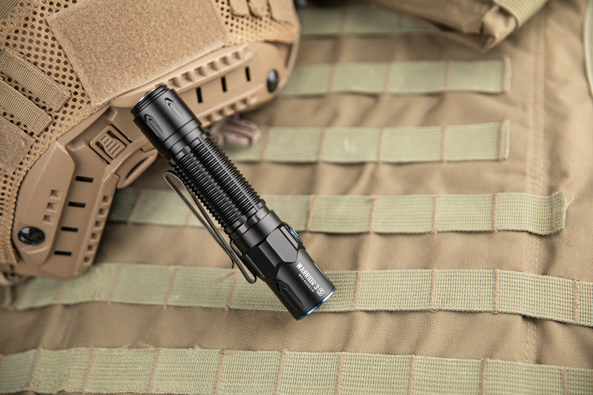 Lampe torche tactique noire Olight Warrior 3S avec clip, sur gilet MOLLE et casque militaire beige.