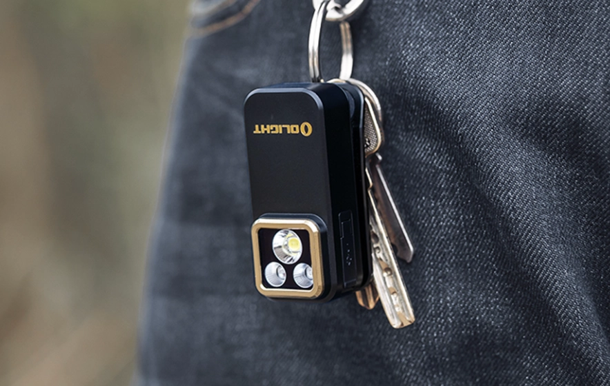 Mini lampe de poche Olight compacte et puissante fixée sur un porte-clés avec des clés, accessoire EDC pratique accroché à la poche d'un jean pour un usage quotidien.