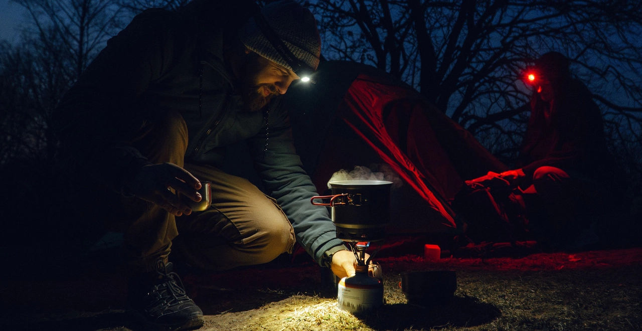 Camping bei Nacht mit Stirnlampe und Gaskocher vor dem Zelt