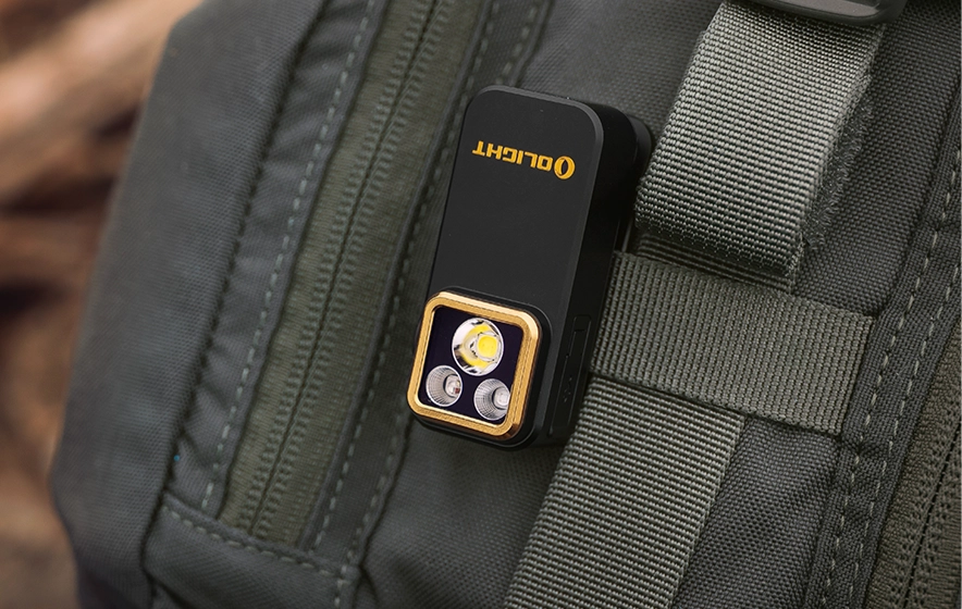 Lampe de poche Olight compacte fixée sur un sac à dos tactique. Éclairage LED portable pour randonnée, camping et EDC. Lampe clip robuste pour aventures en plein air et survie.
