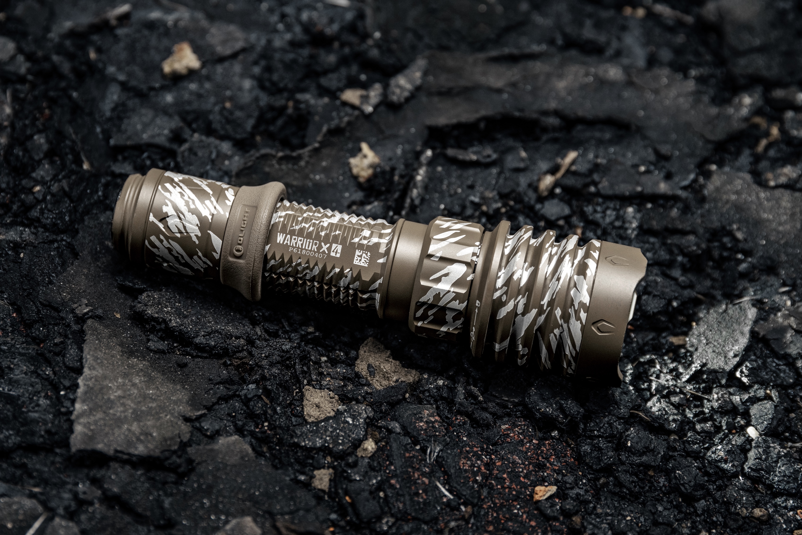 Olight Warrior X 4 taktische LED-Taschenlampe in Tarnmuster-Optik auf rauer Oberfläche.