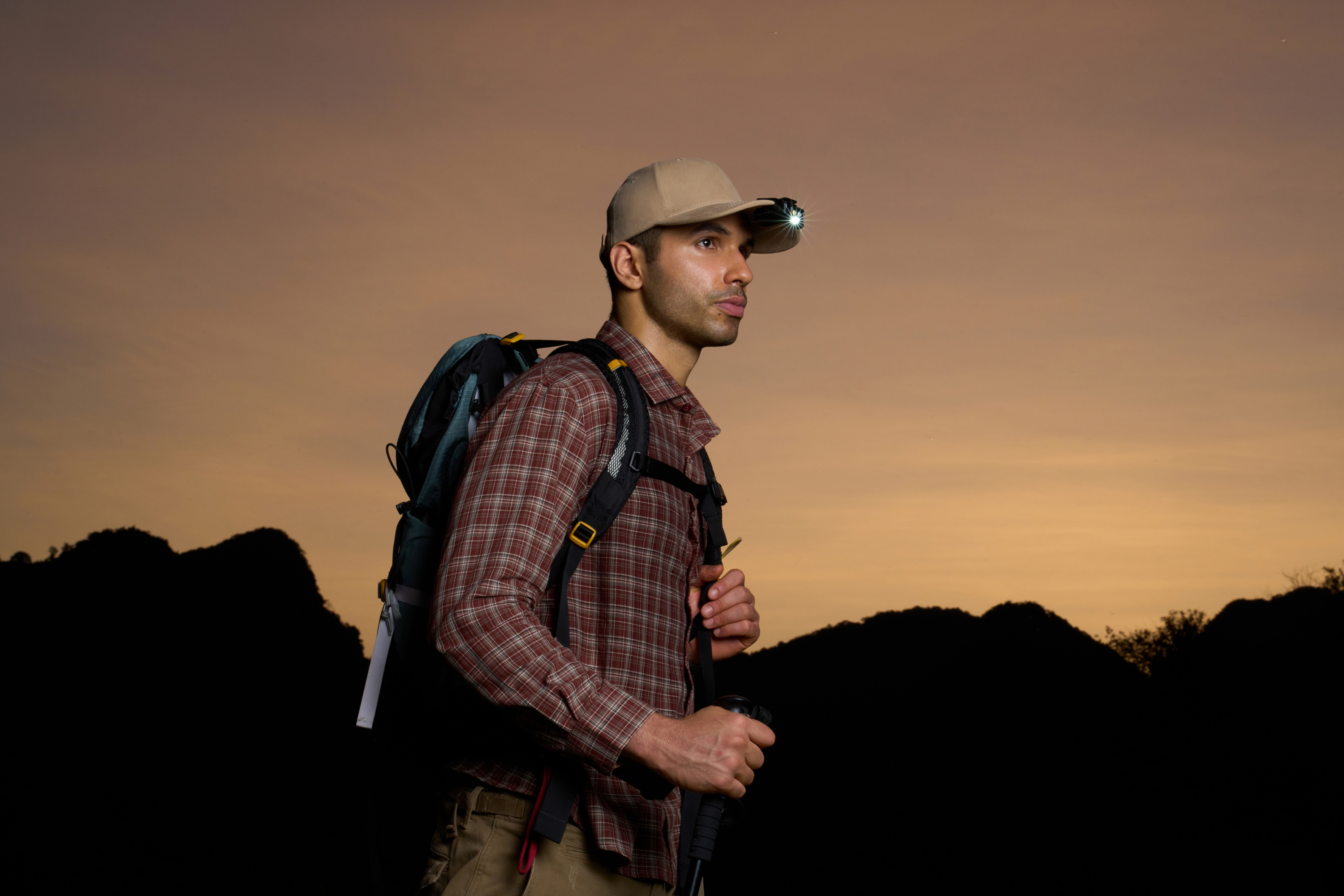 Hiker with backpack and headlamp on cap at sunset