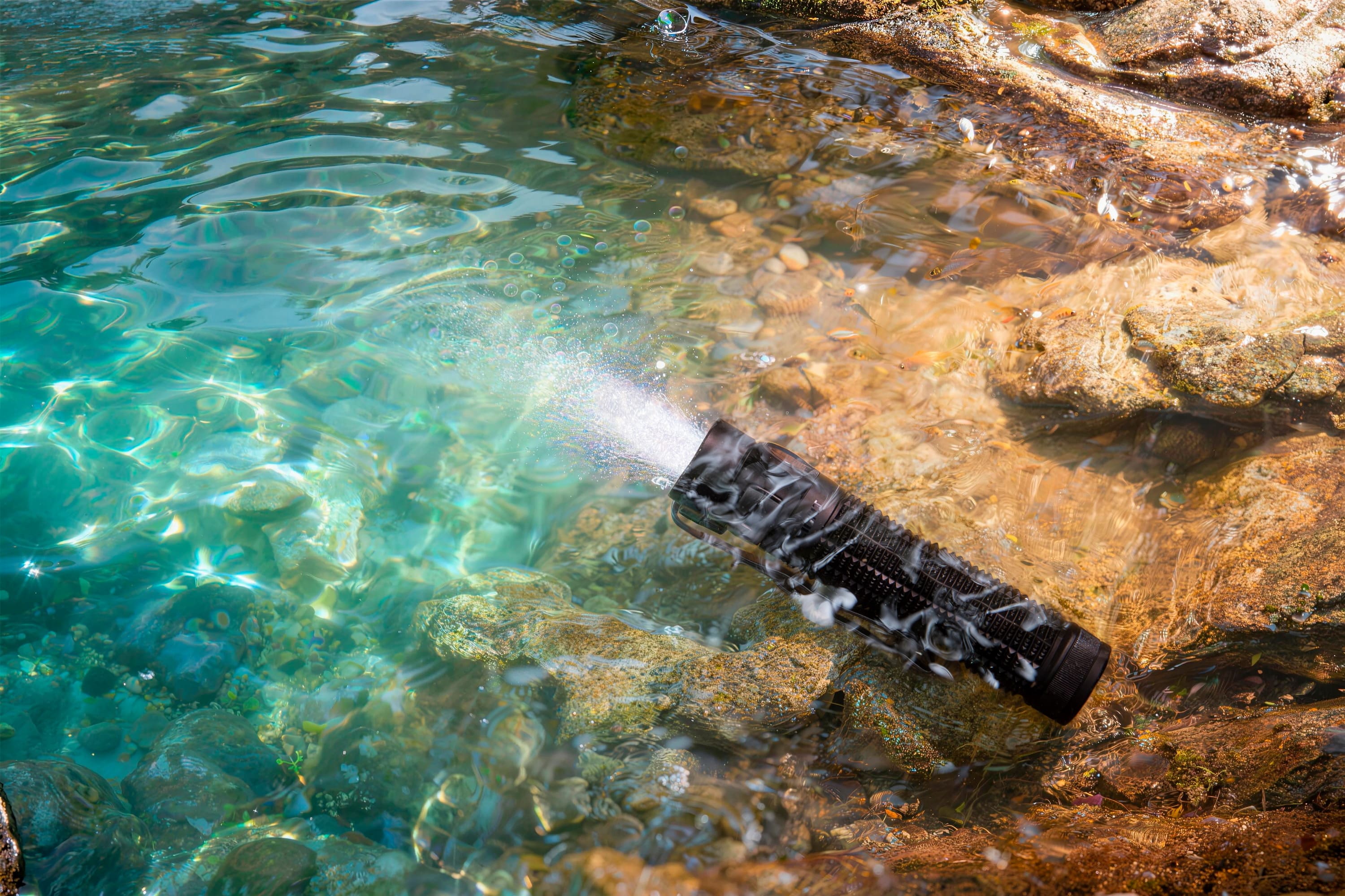 Waterproof tactical flashlight submerged in a clear rocky stream
