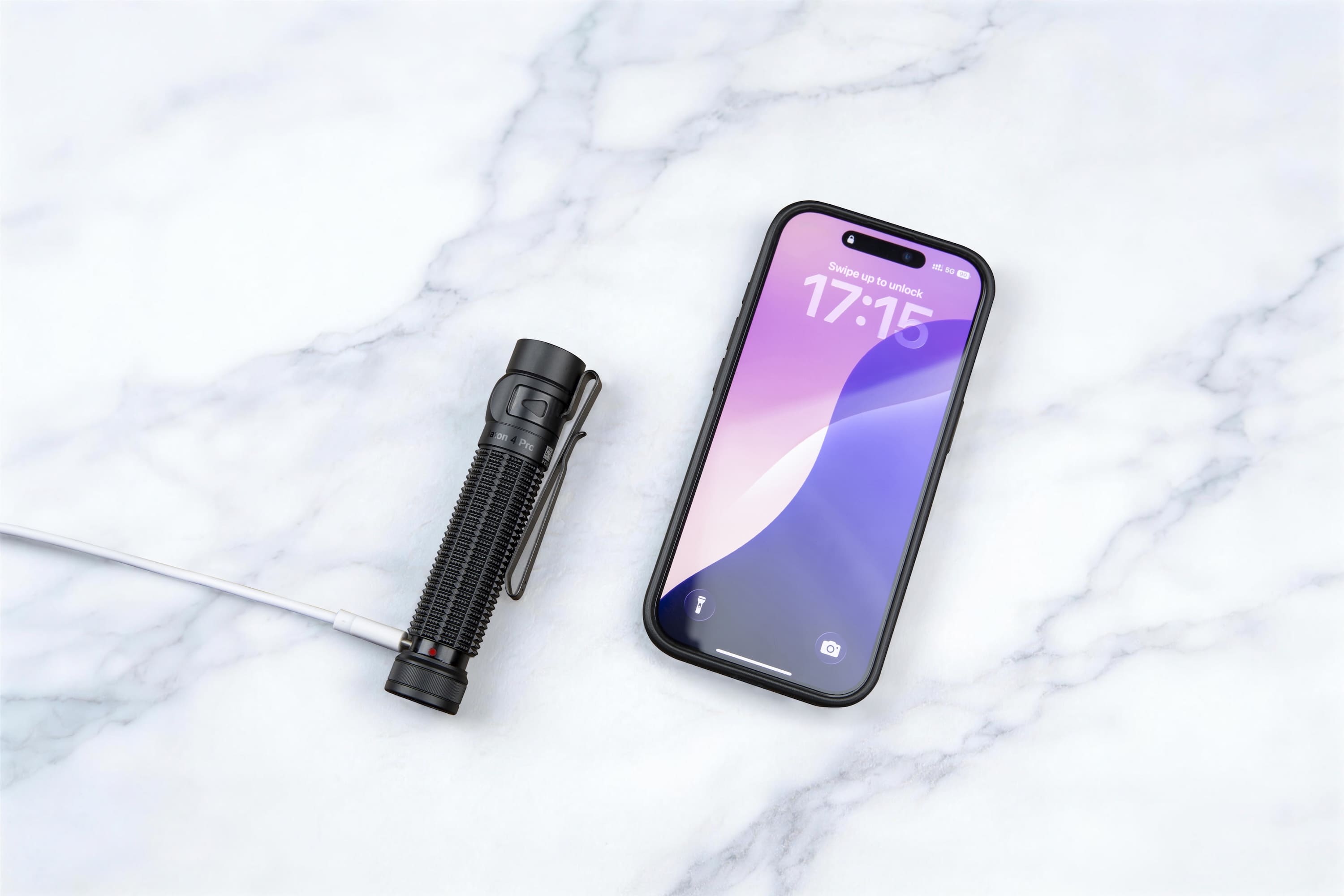 Kompakte LED-Taschenlampe neben Smartphone auf Marmor