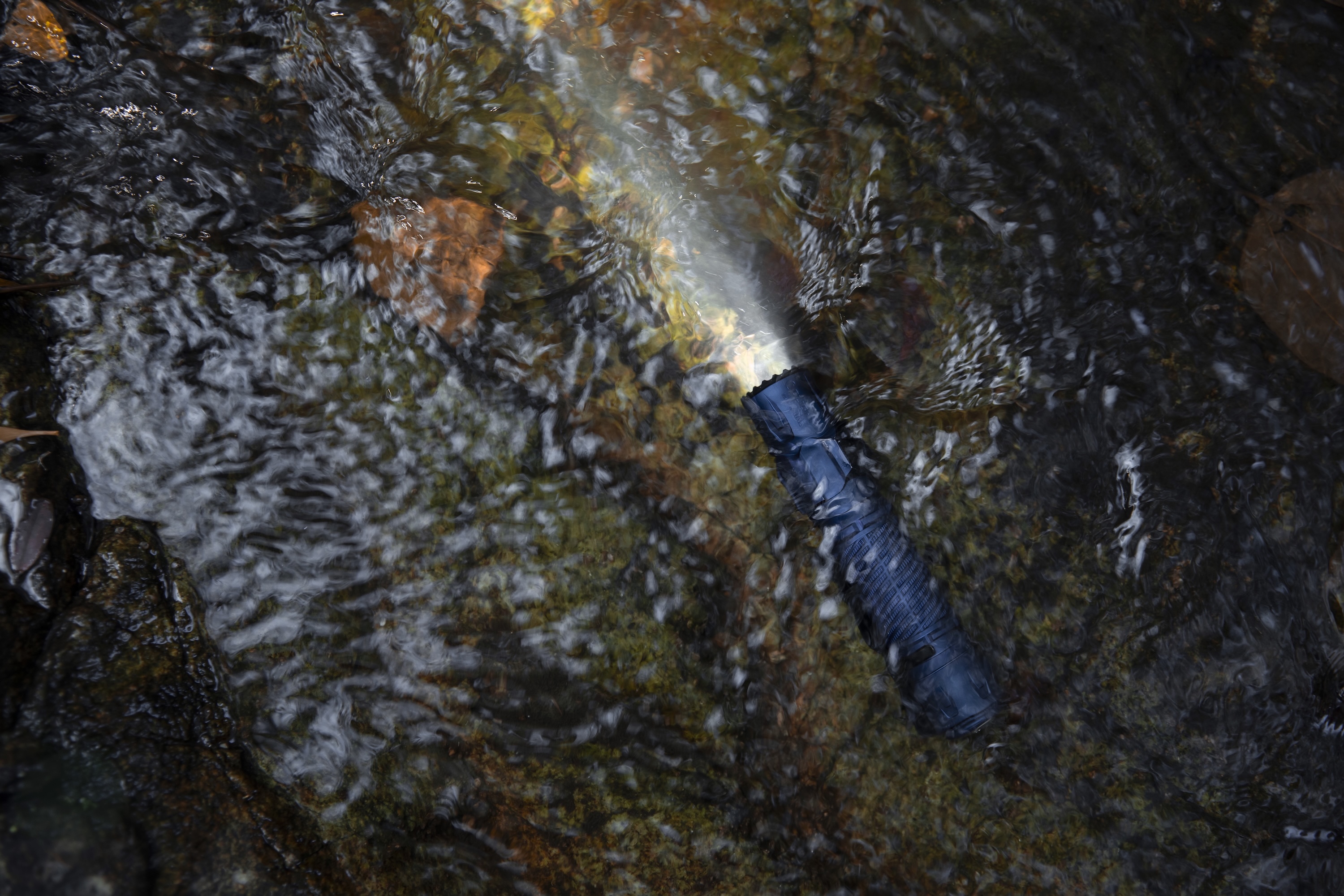Wasserdichte Taschenlampe in fließendem Wasser eines Baches, beleuchtet den felsigen Untergrund mit hellem Lichtstrahl.