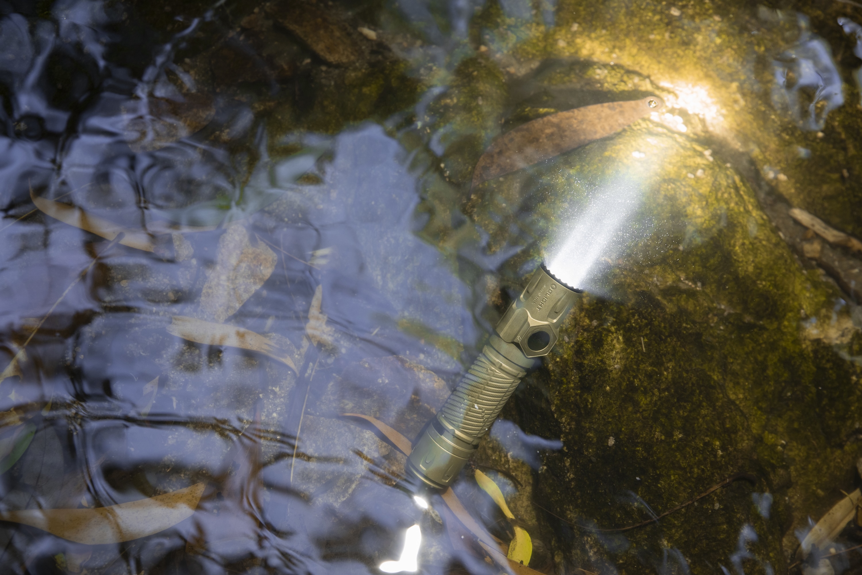 Wasserdicht Taschenlampe leuchtet hell unter Wasser auf moosigem Grund.