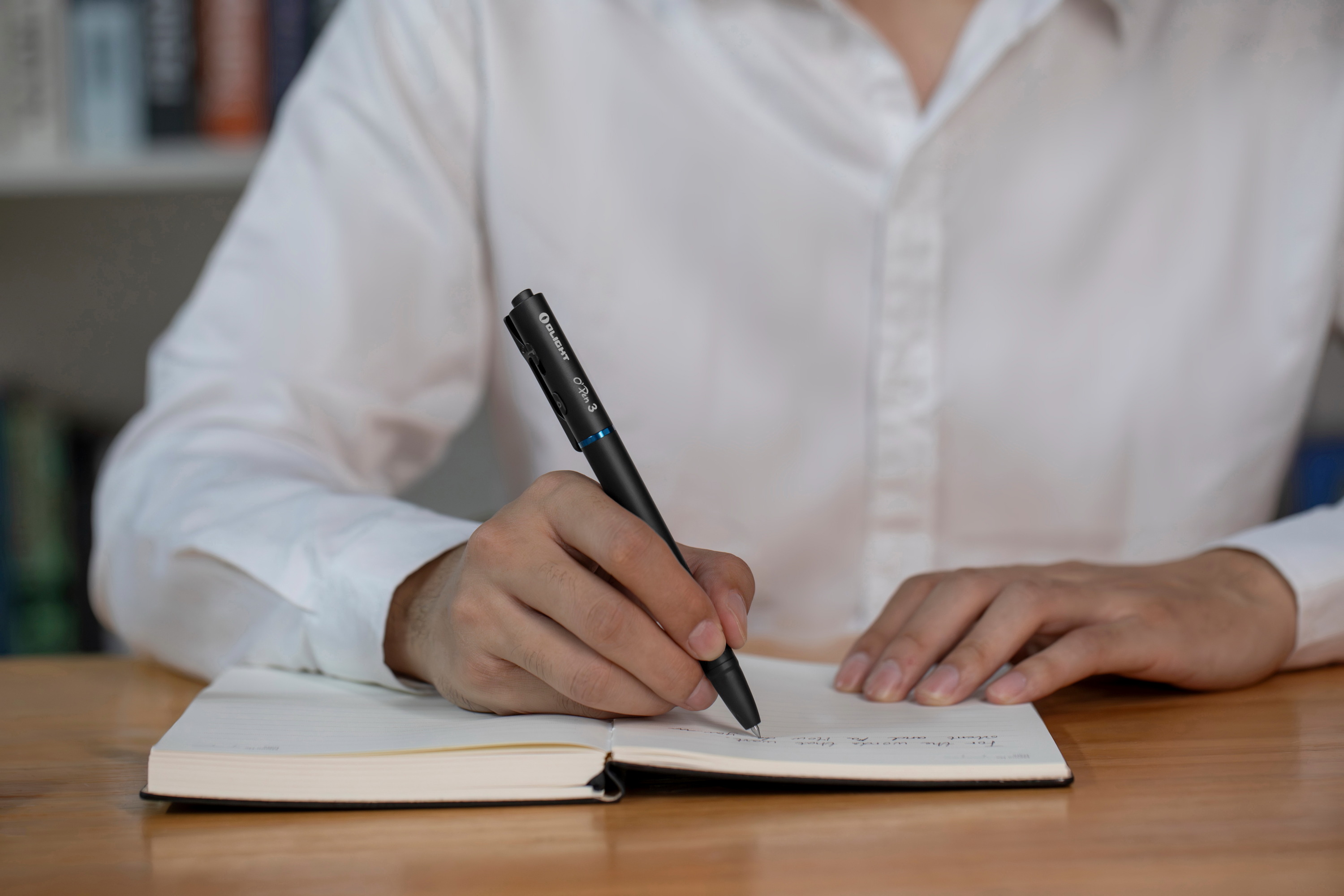 Persona escribiendo en un cuaderno con el bol&iacute;grafo t&aacute;ctico Olight Open 3 negro en una oficina.