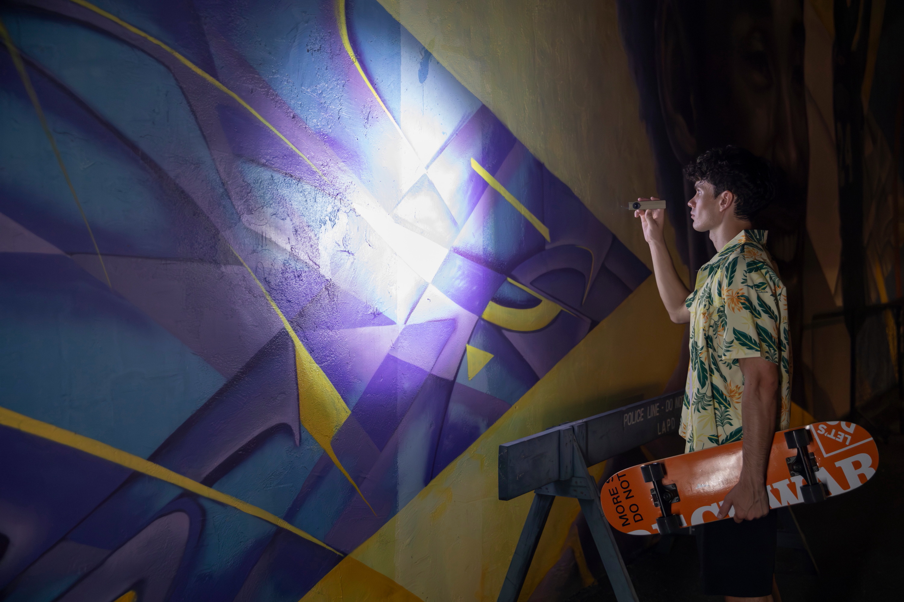 Skater mit Skateboard leuchtet nachts mit einer Taschenlampe auf ein buntes Graffiti-Wandbild.