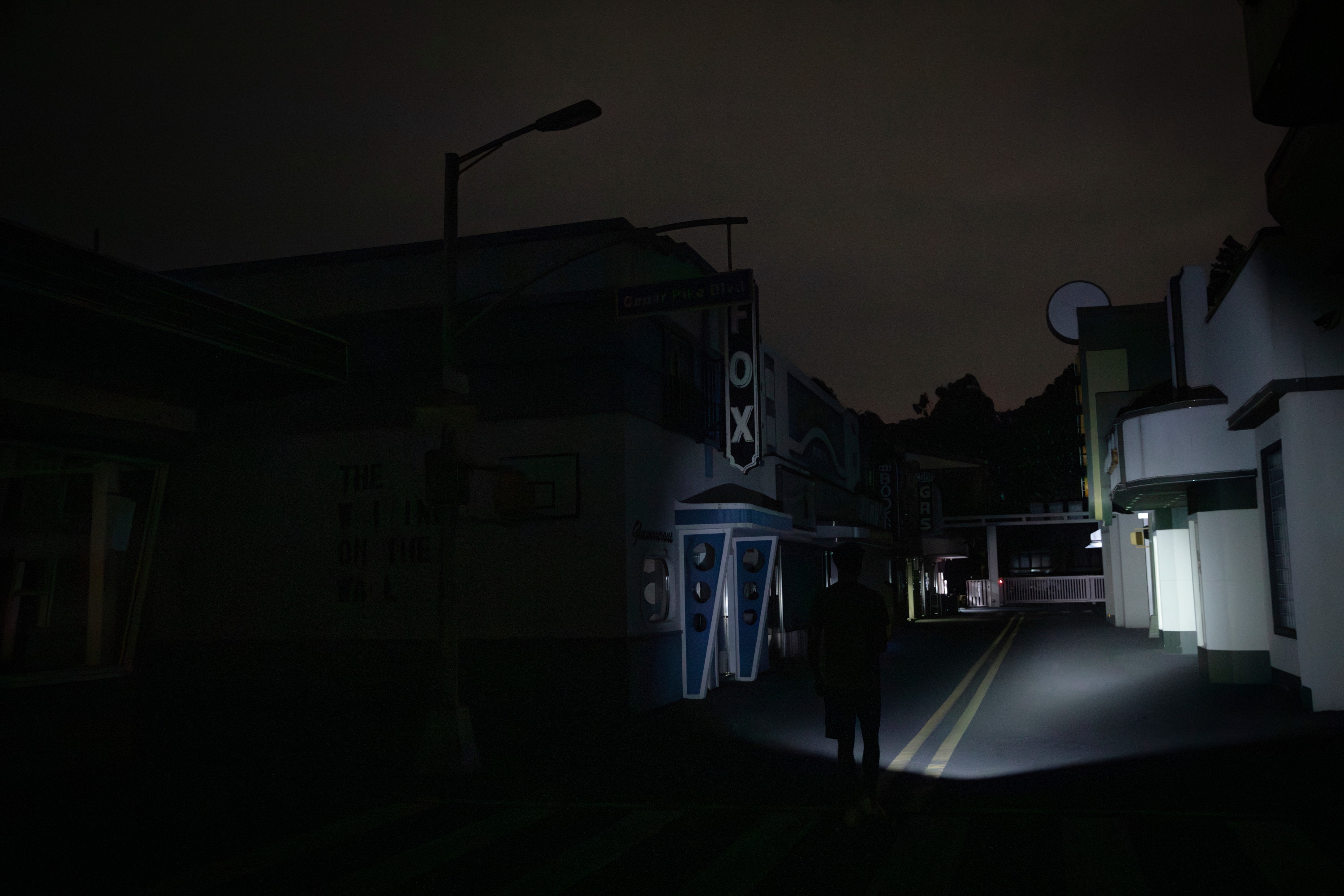 Man walking down a dark, empty city street at night with a flashlight