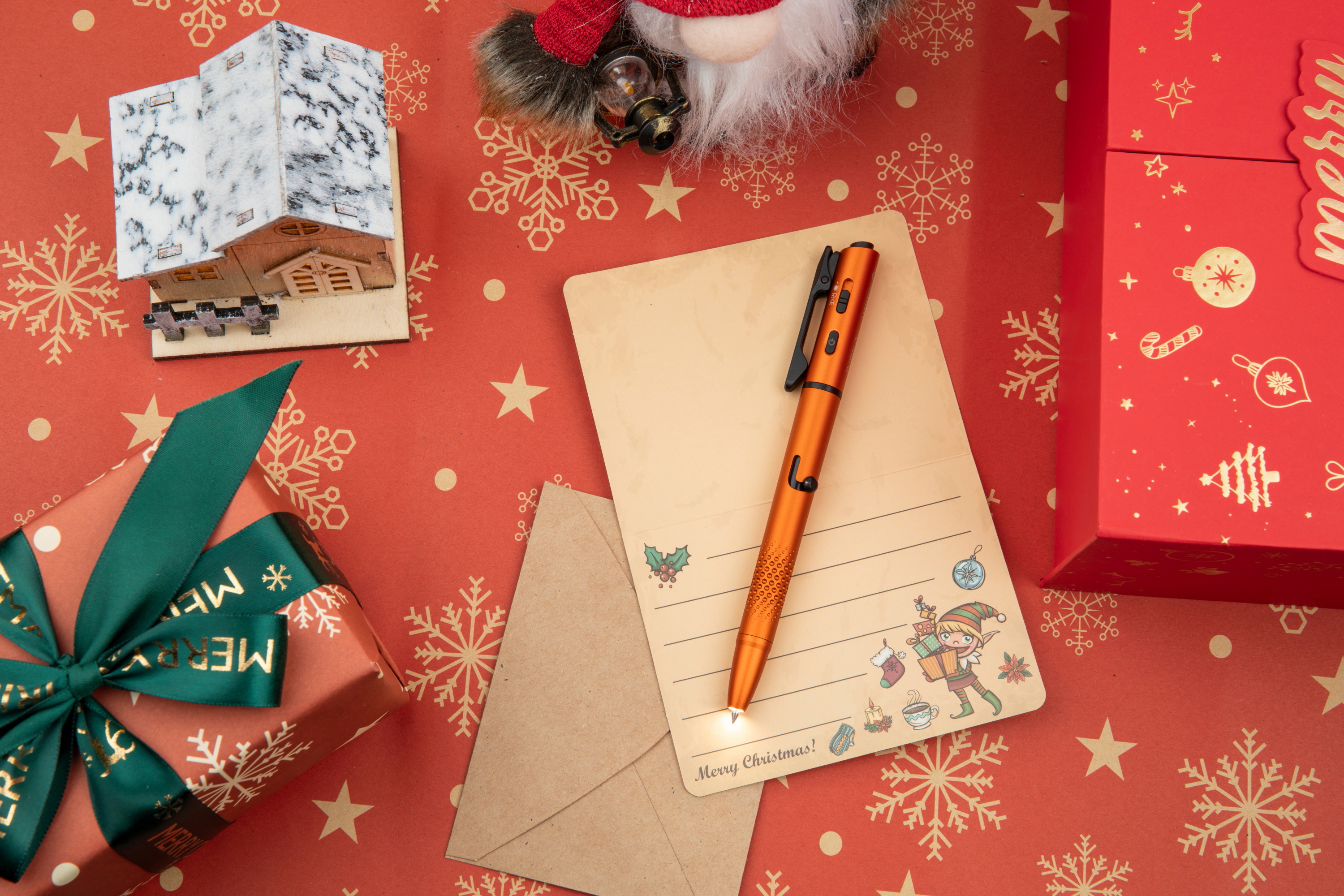 Festive Christmas flat lay with wrapped gifts and a glowing orange pen, arranged on a red background with golden snowflakes.