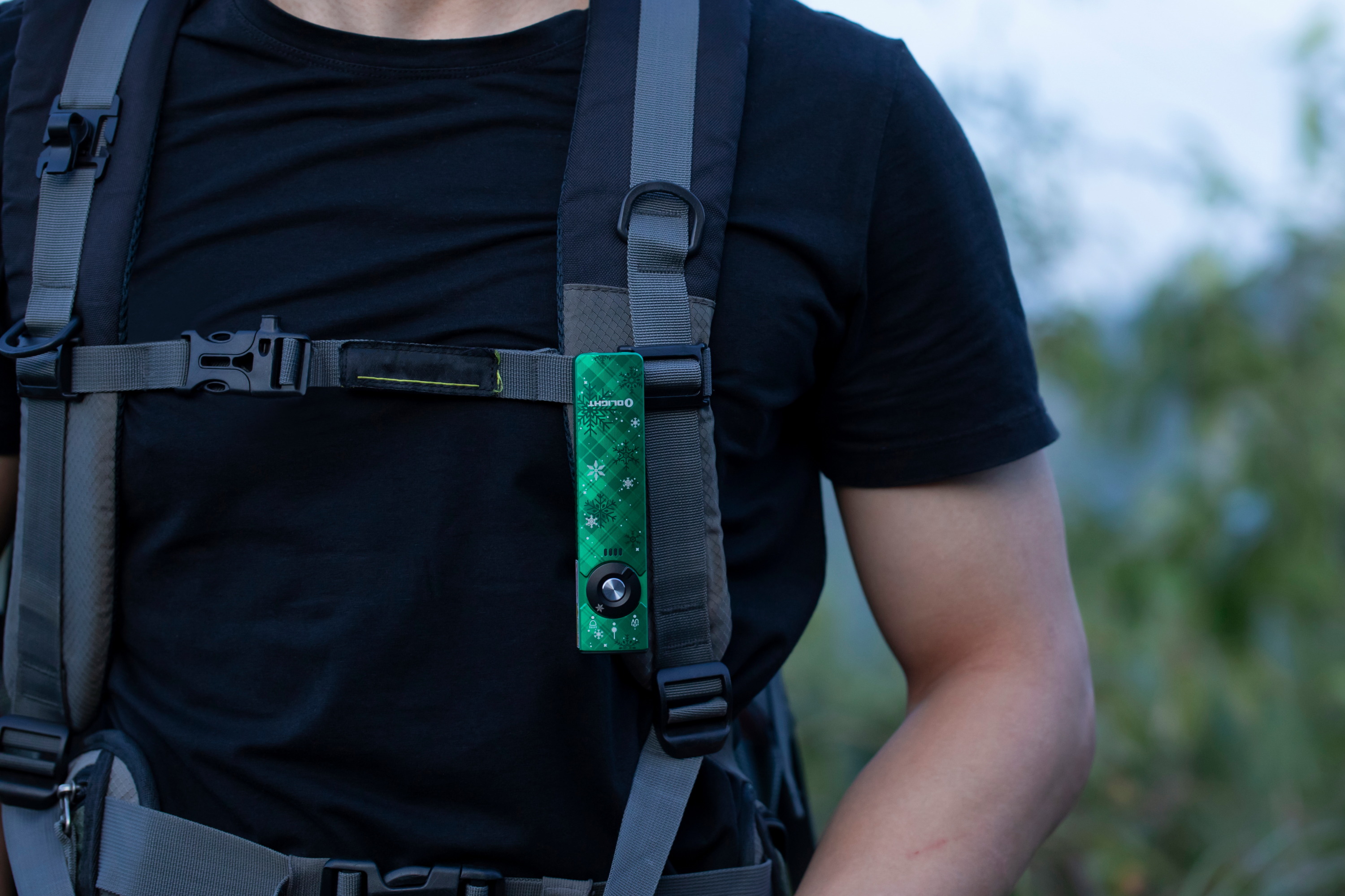 Grüne Olight Taschenlampe mit Schneeflockenmuster am Rucksackgurt eines Wanderers.