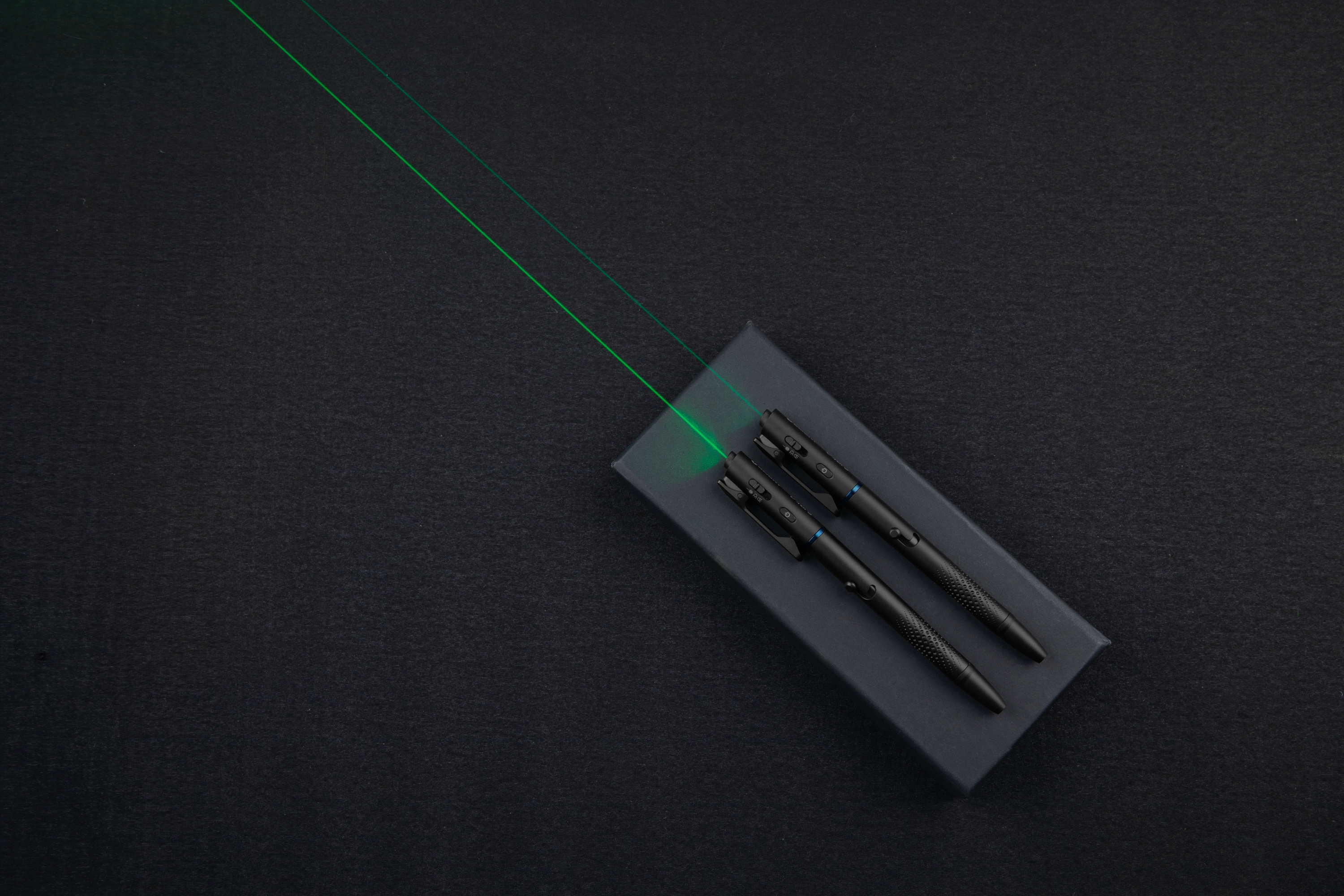 블랙 배경 위에서 초록색 빔을 발사하는 두 개의 고출력 그린 레이저 포인터 및 전술 펜 세트.