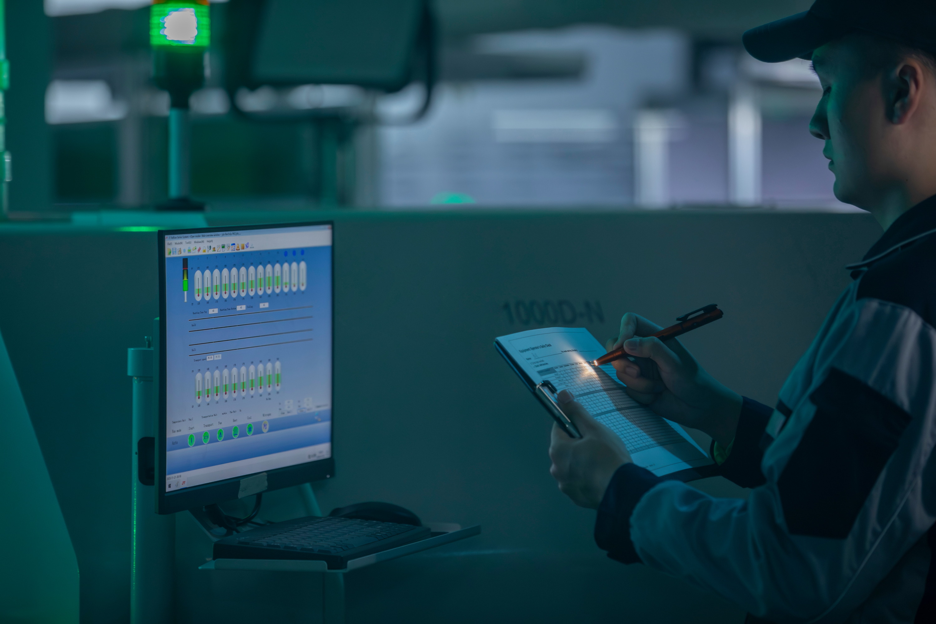 Technicien industriel surveillant les donn&eacute;es de production sur un &eacute;cran de contr&ocirc;le num&eacute;rique et prenant des notes dans une usine intelligente.