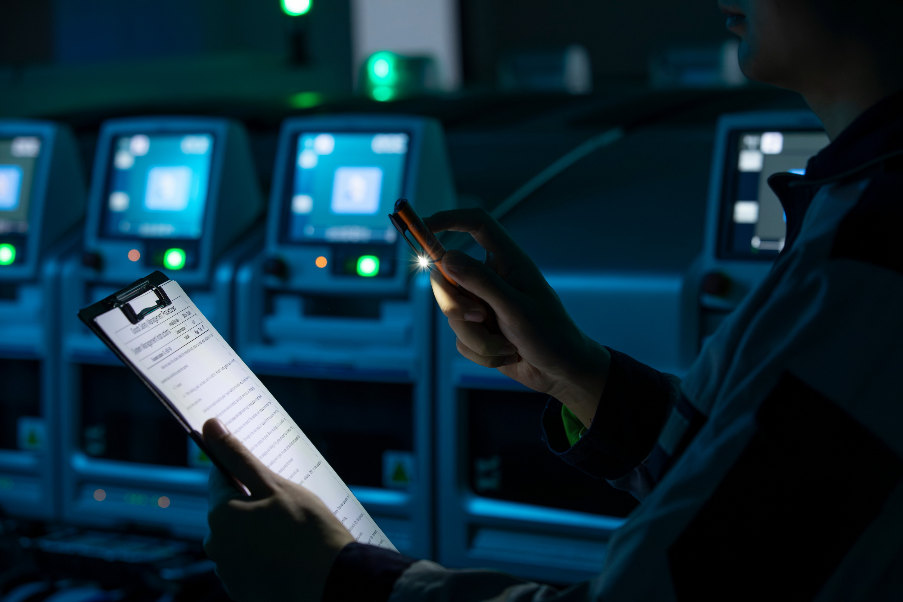 데이터 센터 제어실에서 클립보드와 손전등을 사용하여 시스템 상태를 점검하고 모니터링하는 전문 엔지니어의 모습.