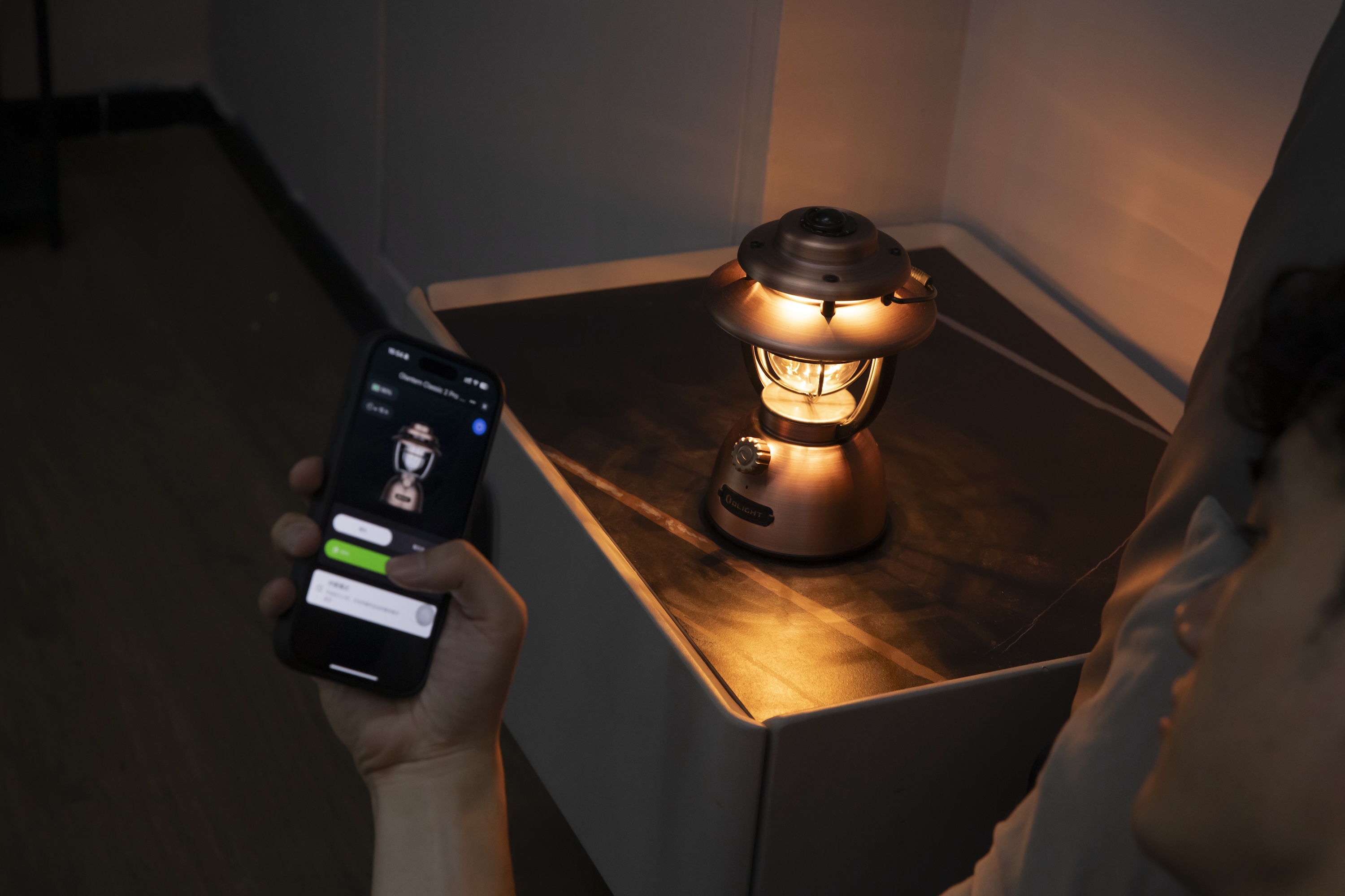 스마트폰 앱으로 Olight 빈티지 랜턴 램프의 따뜻한 빛을 조절하는 모습. 아늑한 침실 분위기 연출.