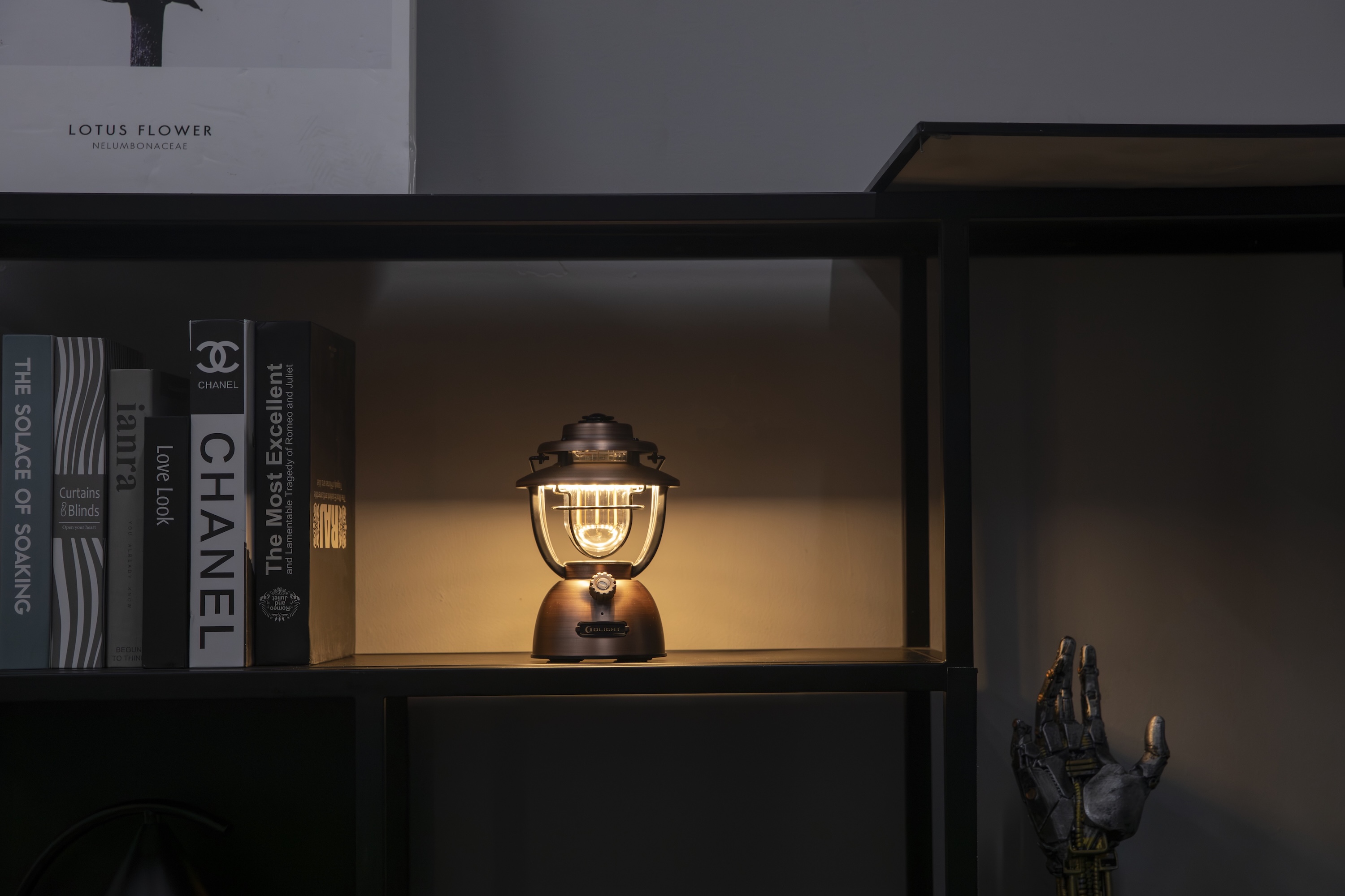 선반 위 빛나는 빈티지 스타일 GOLIGHT 랜턴 조명. 책과 로봇 손 장식과 어우러져 아늑한 실내 분위기를 연출합니다.