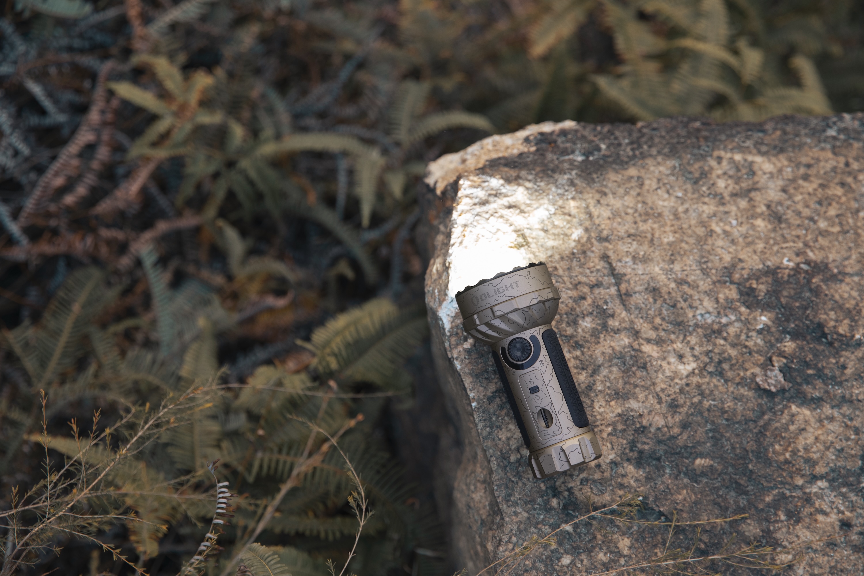 Olight迷彩柄懐中電灯が岩を明るく照らす、アウトドアのシーン。