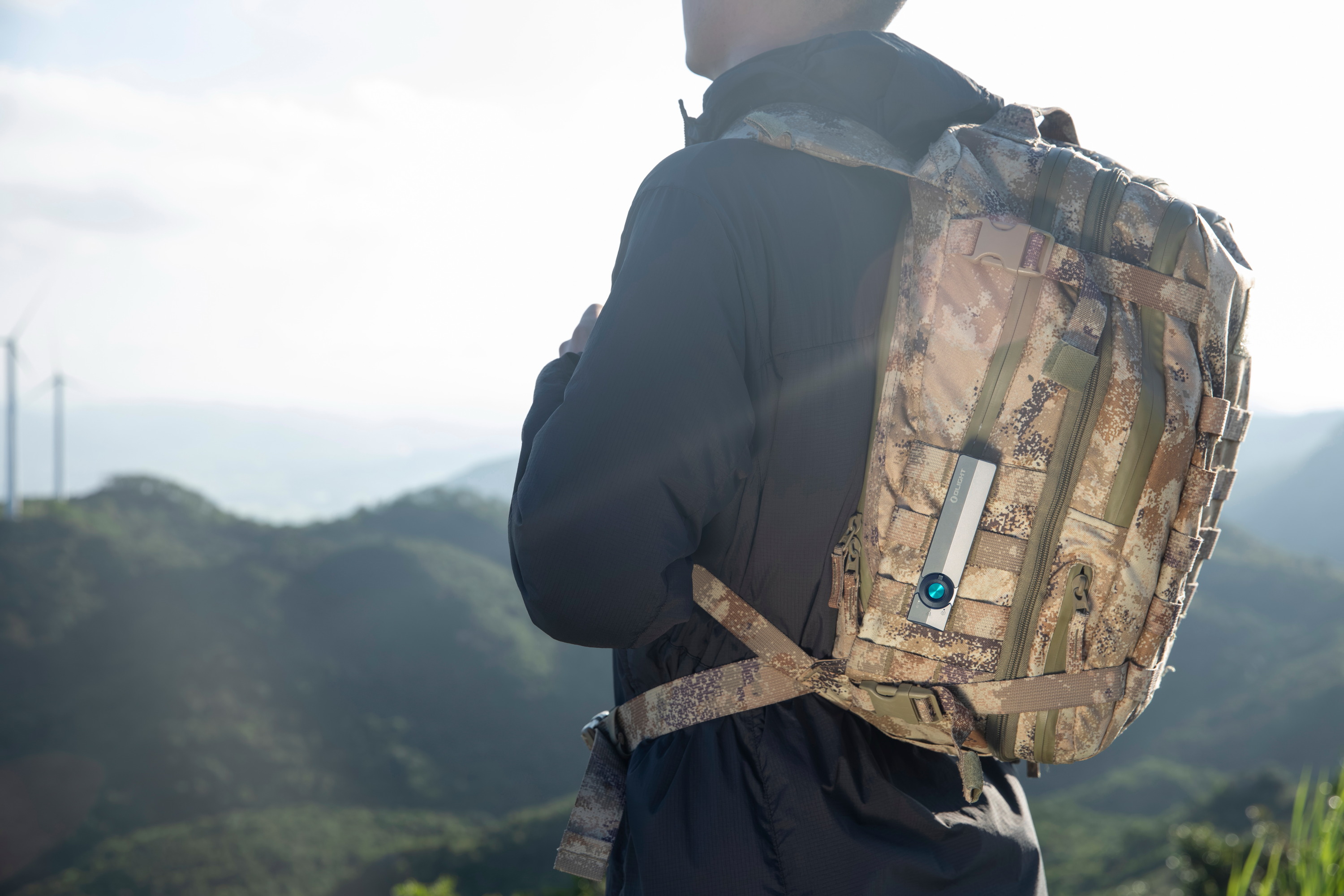 Randonneur avec sac &agrave; dos tactique camouflage et lampe torche Olight compacte haute performance pour la randonn&eacute;e et le plein air en montagne.