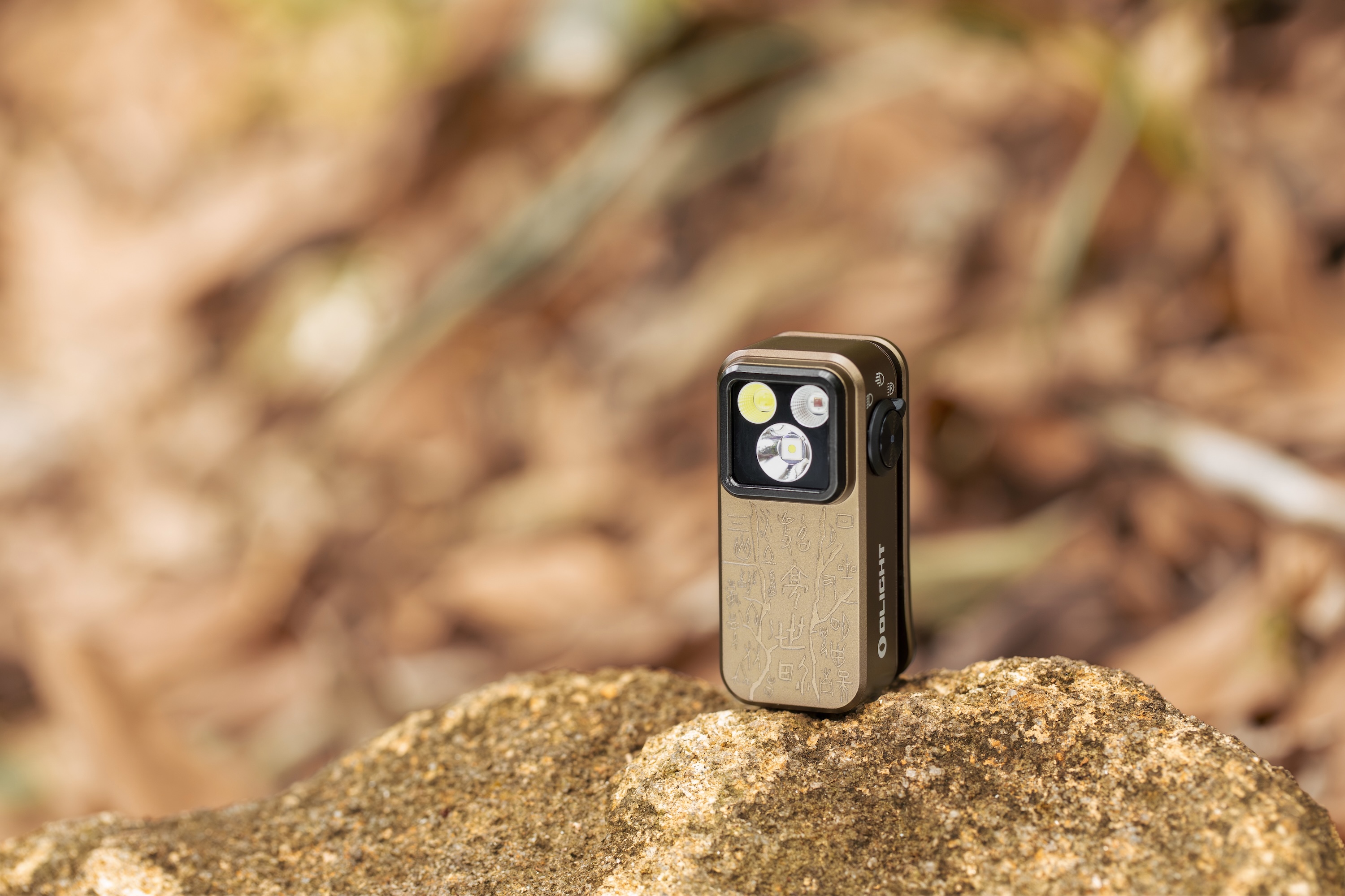 Close-up of Olight Oclip Pro with laser-etched tree patterns on a brown body, showing its multi-LED head in a forest background.