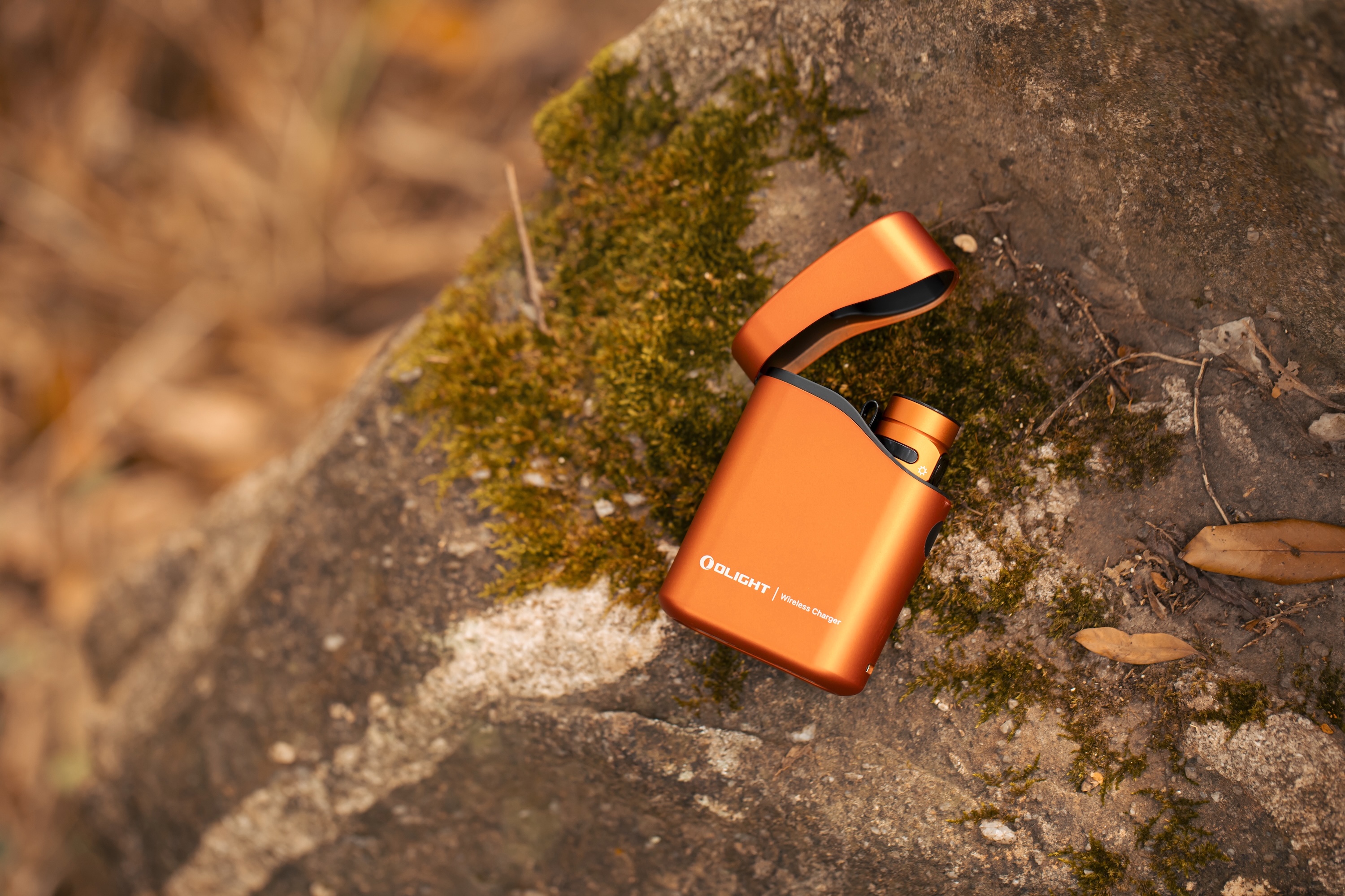 Olightオレンジ色ワイヤレス充電器が苔むした岩上に置かれ、開いたケースから中のデバイスが見える。