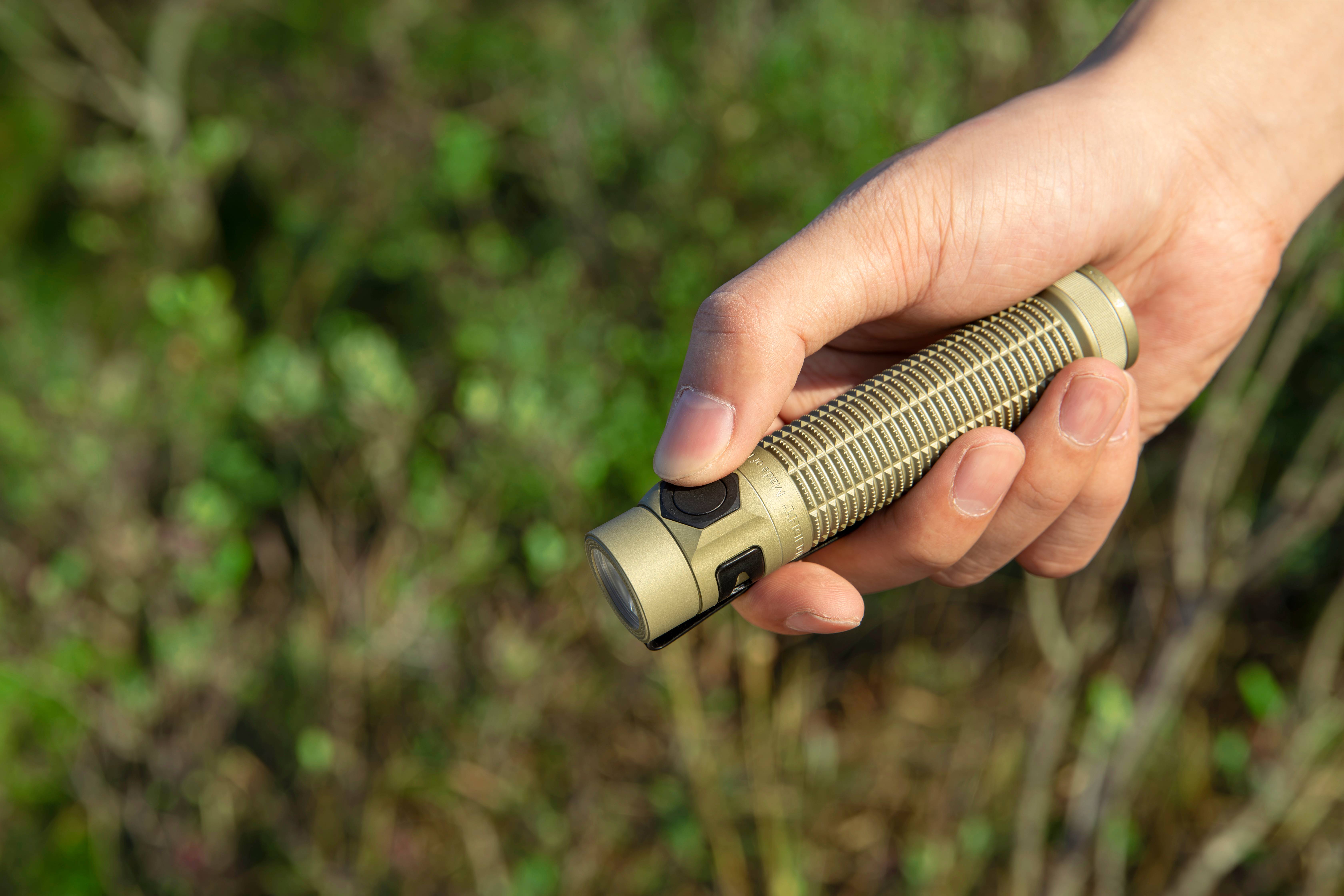 Holding a compact tan tactical EDC flashlight outdoors
