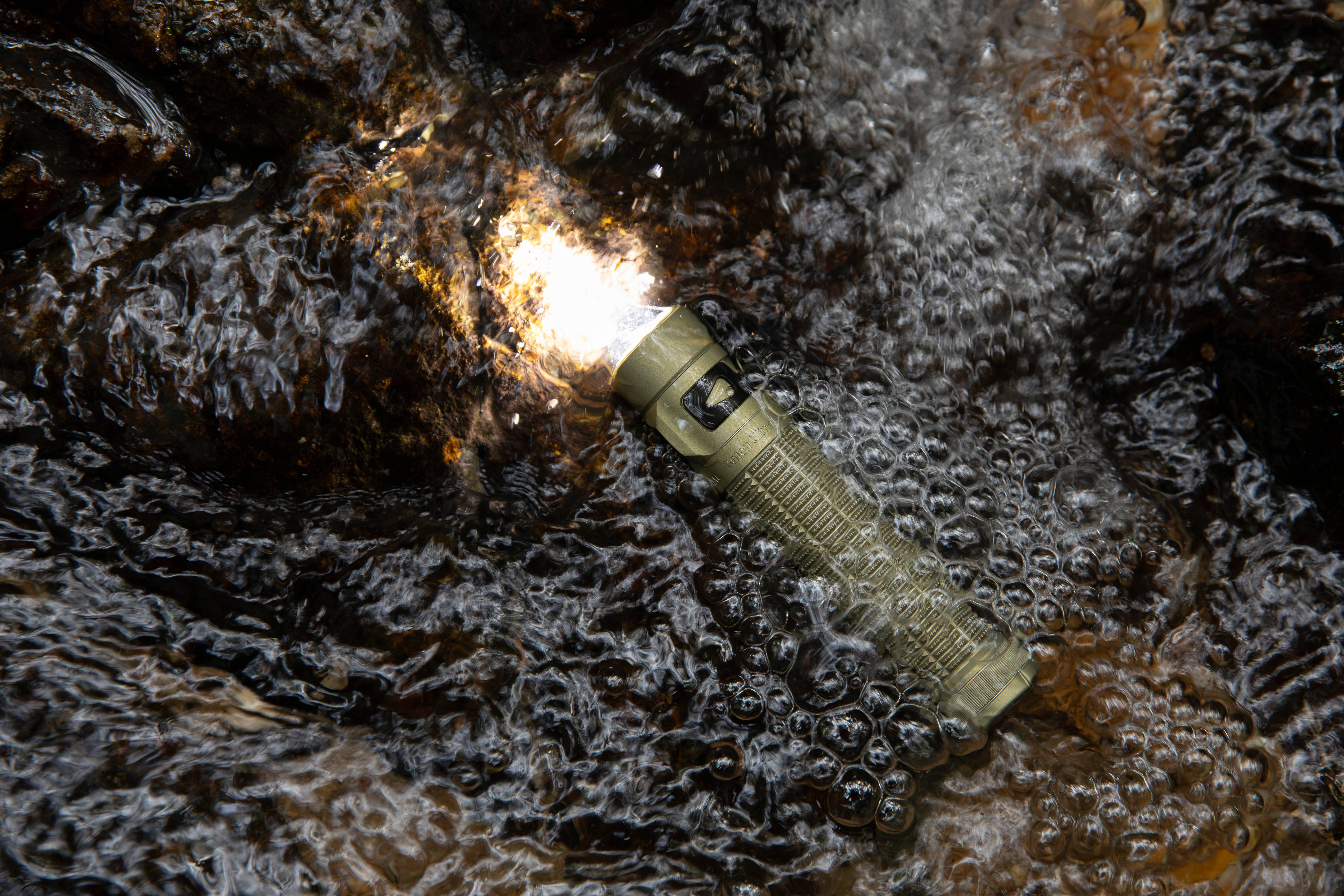 Waterproof Olight Baton EDC flashlight submerged in a flowing stream, demonstrating IPX8 water resistance and durability for outdoor camping, hiking, and tactical use.