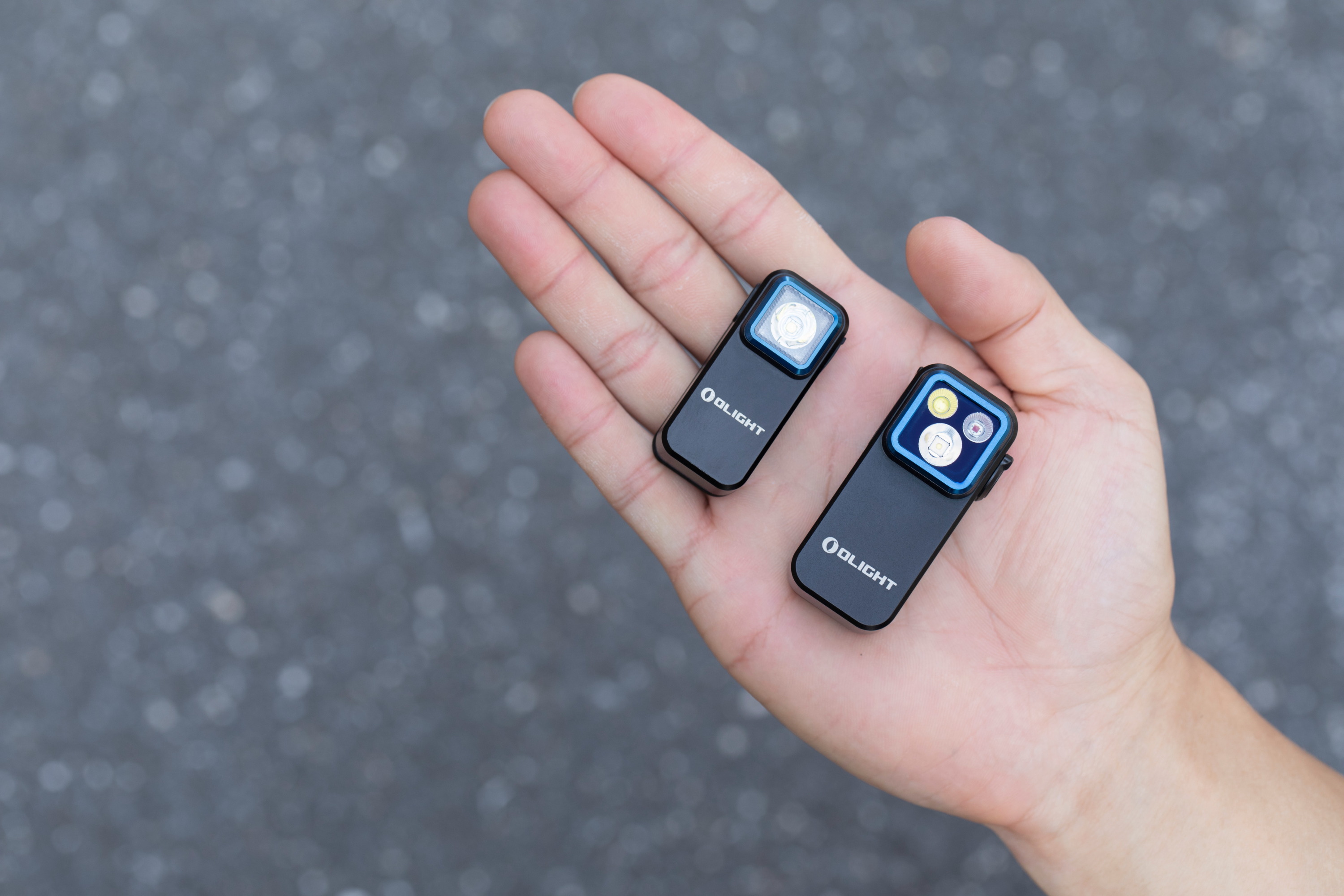 Zwei kompakte schwarze Olight Clip LED-Taschenlampen auf einer Handfl&auml;che