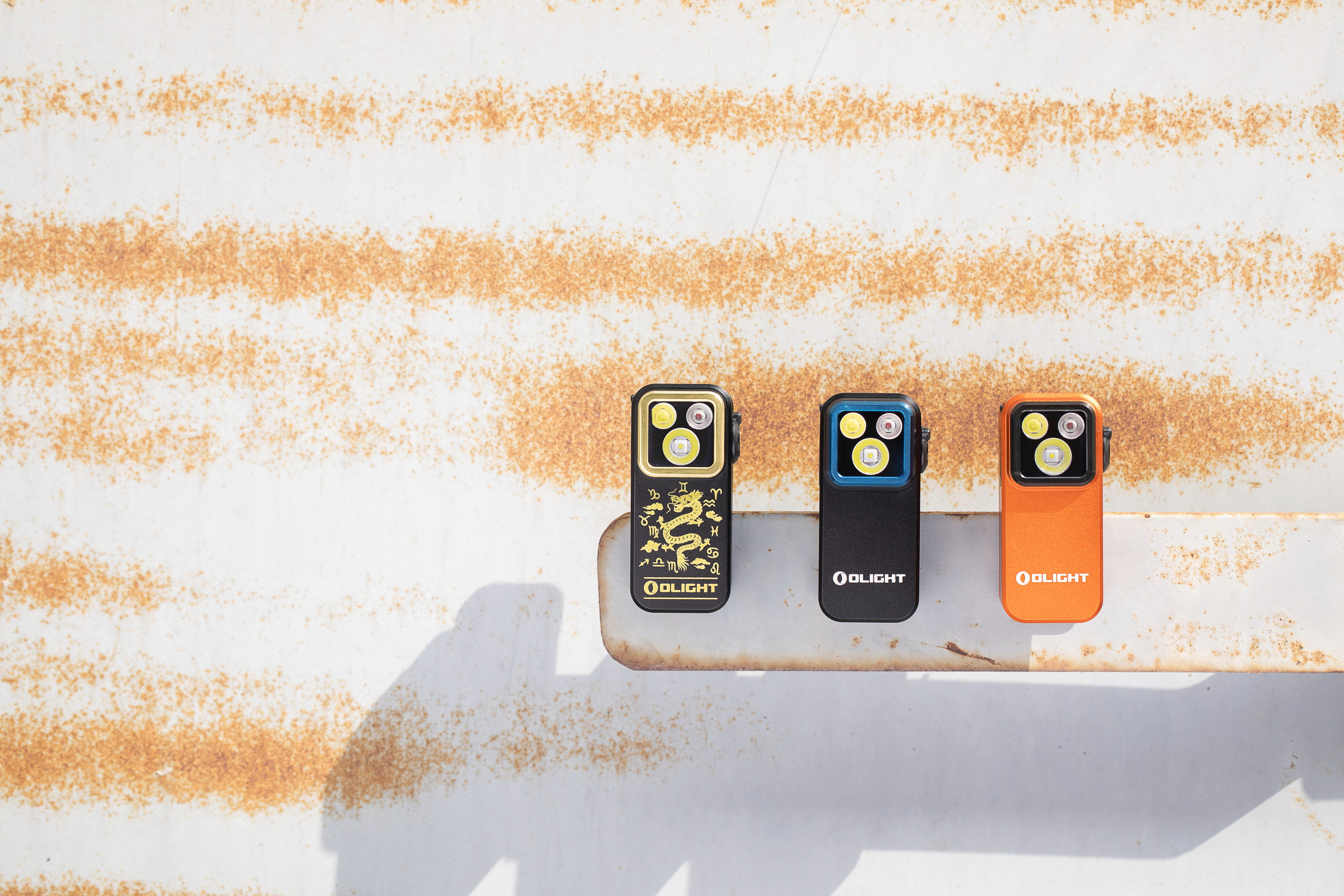 오라이트 EDC 플래시라이트(용 에디션, 블랙, 오렌지)가 녹슨 표면에 놓여 있는 모습.