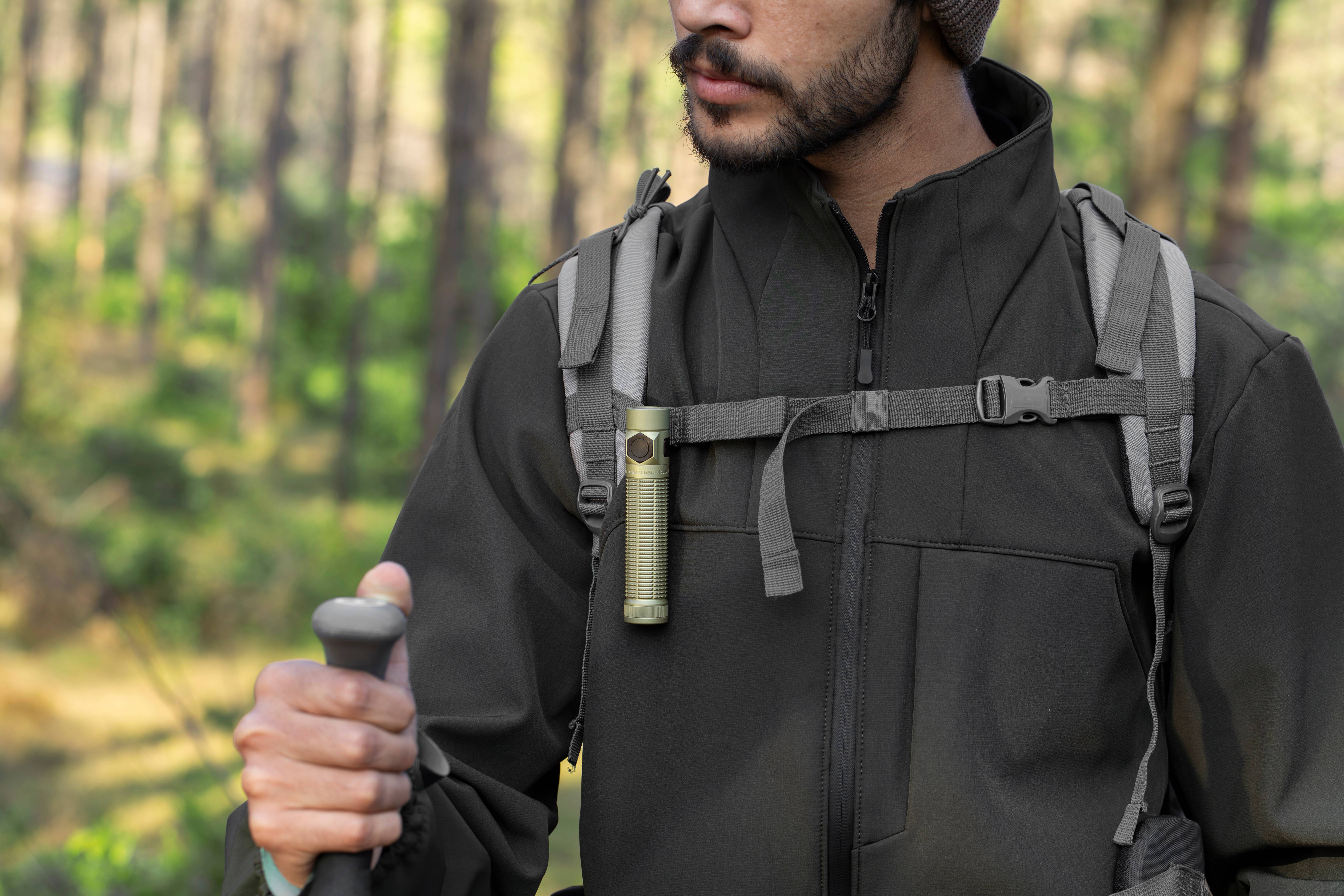 Hombre haciendo senderismo con una linterna LED compacta enganchada a la correa de su mochila en el bosque.