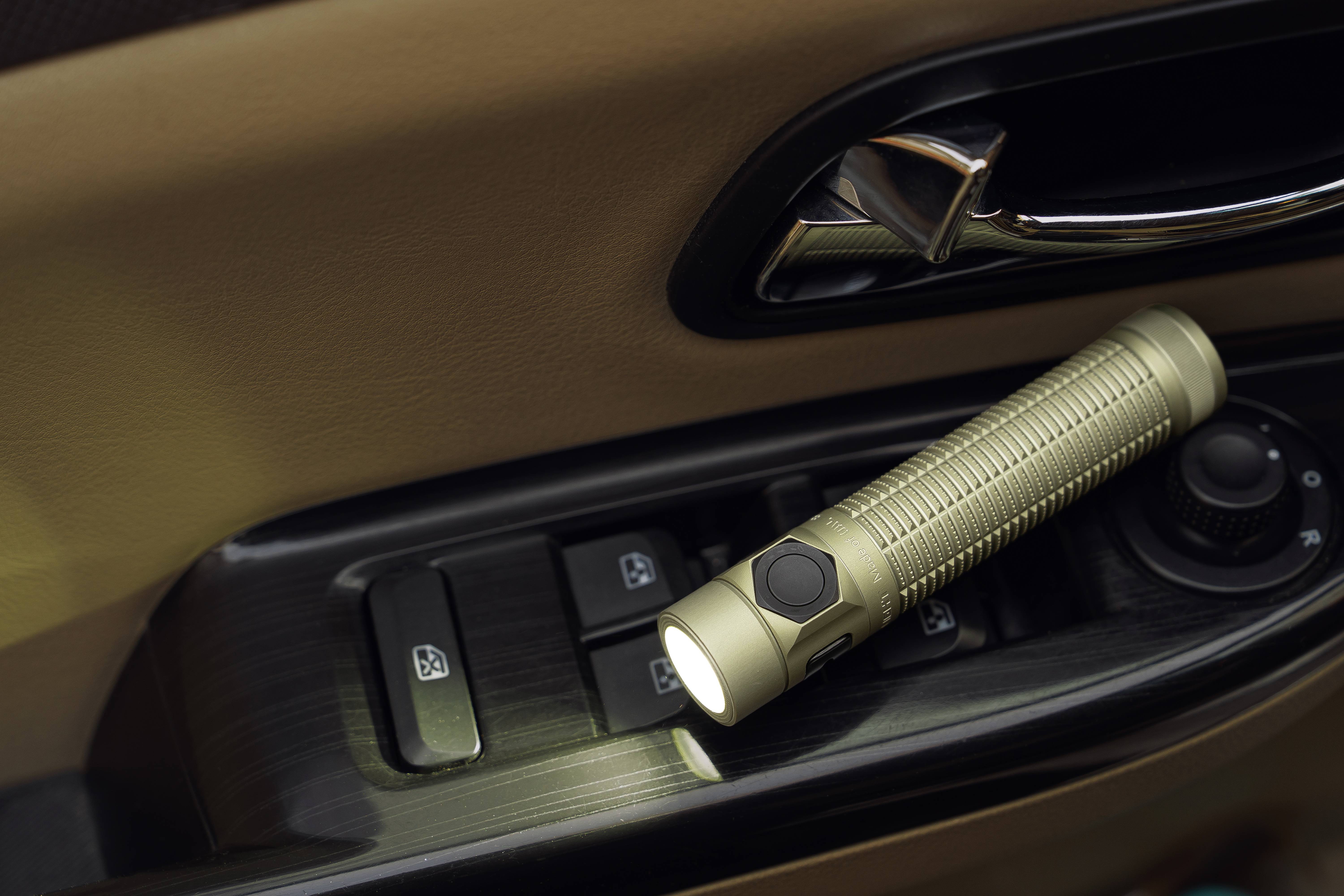 Lampe torche LED compacte de couleur champagne allumée sur l'accoudoir d'une portière de voiture. Équipement EDC indispensable pour la sécurité automobile et l'éclairage de secours nocturne.