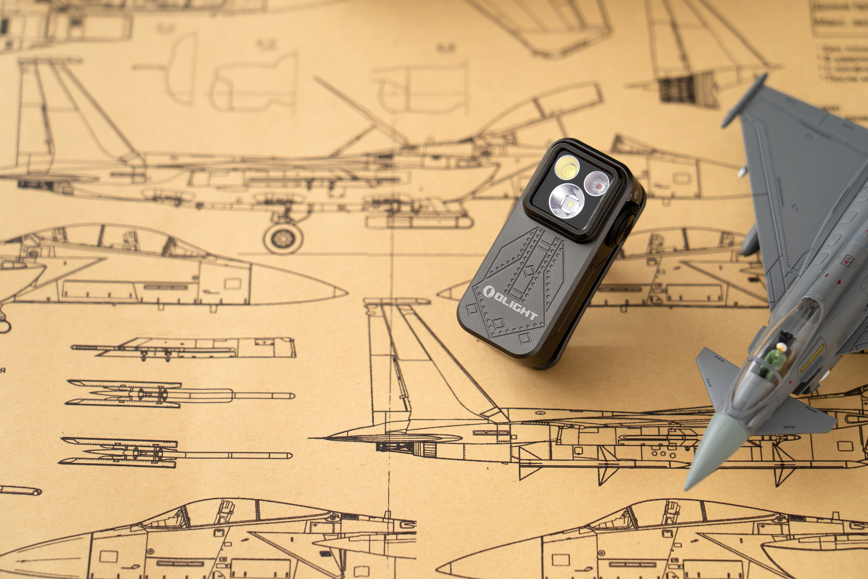 Olight Arkfeldフラッシュライトと戦闘機の模型、航空機設計図が描かれた背景