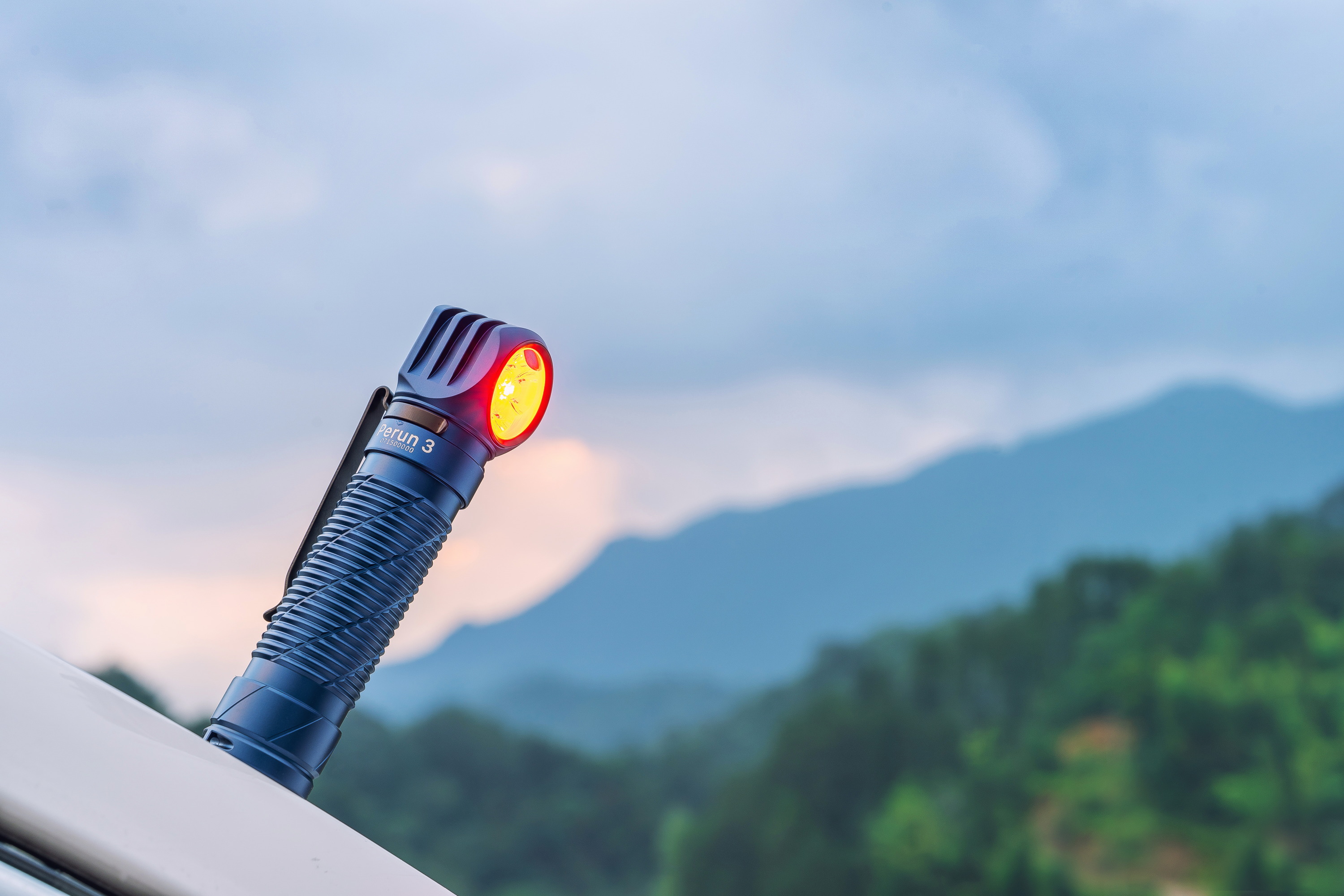 Linterna Olight Perun 3 azul con luz roja en un paisaje de montaña al atardecer.