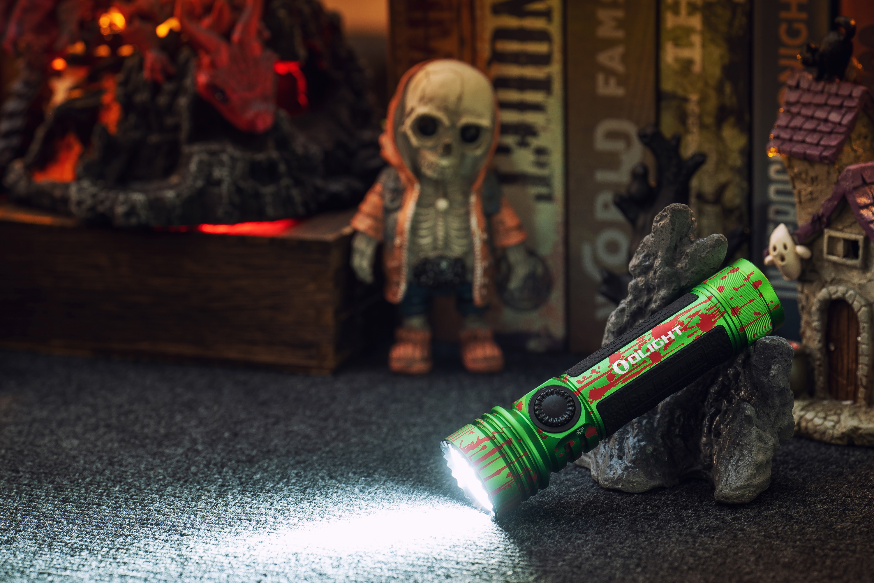 Linterna Olight verde de Halloween con salpicaduras de sangre, iluminando un esqueleto y una casa embrujada en una ambientación de terror.