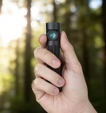 Kompakte schwarze LED-Taschenlampe in der Hand gehalten im sonnigen Wald – ideal für Outdoor, Wandern und Camping.