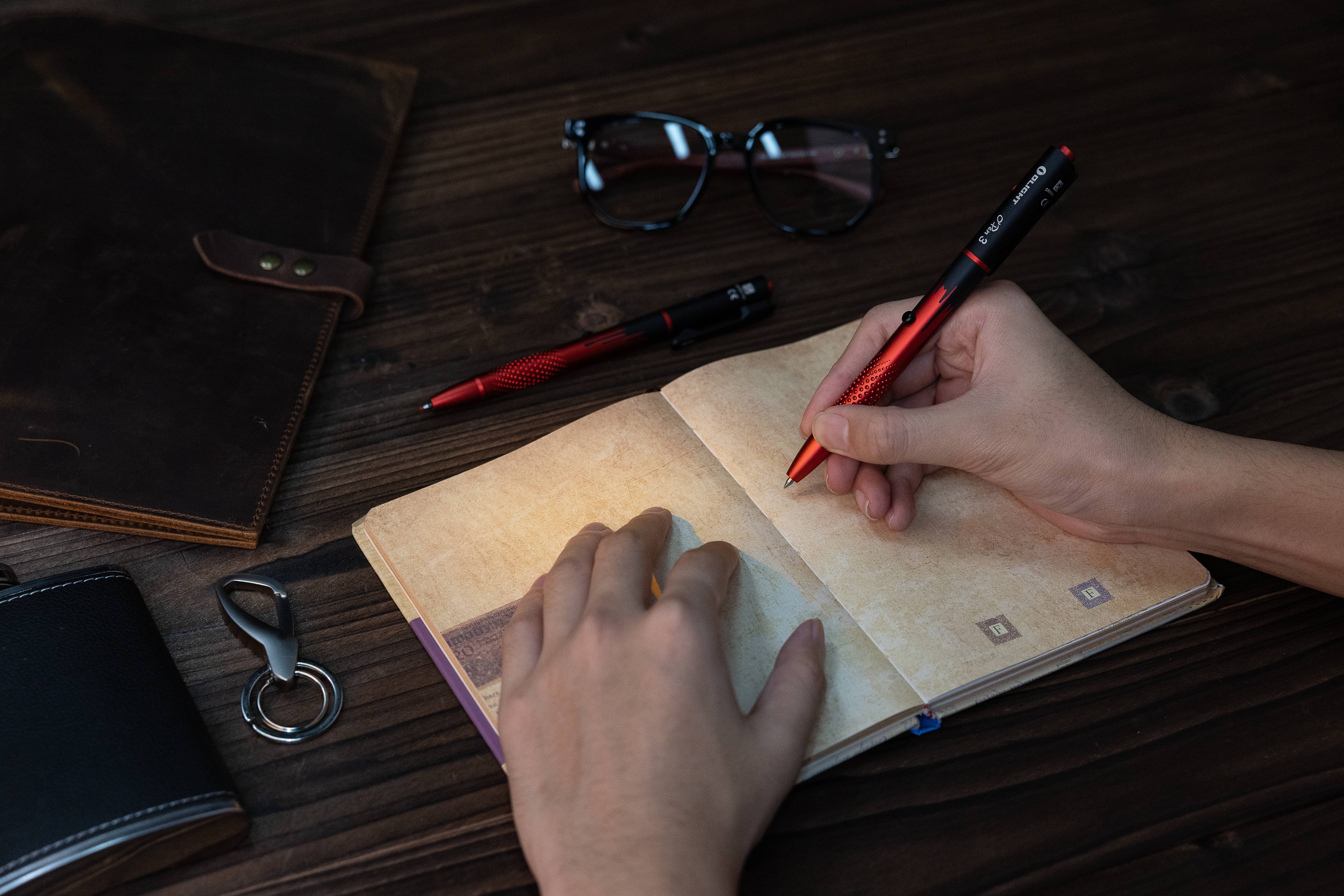 Lampe stylo Olight O'Pen 3 utilis&eacute;e pour &eacute;crire sur un carnet en cuir