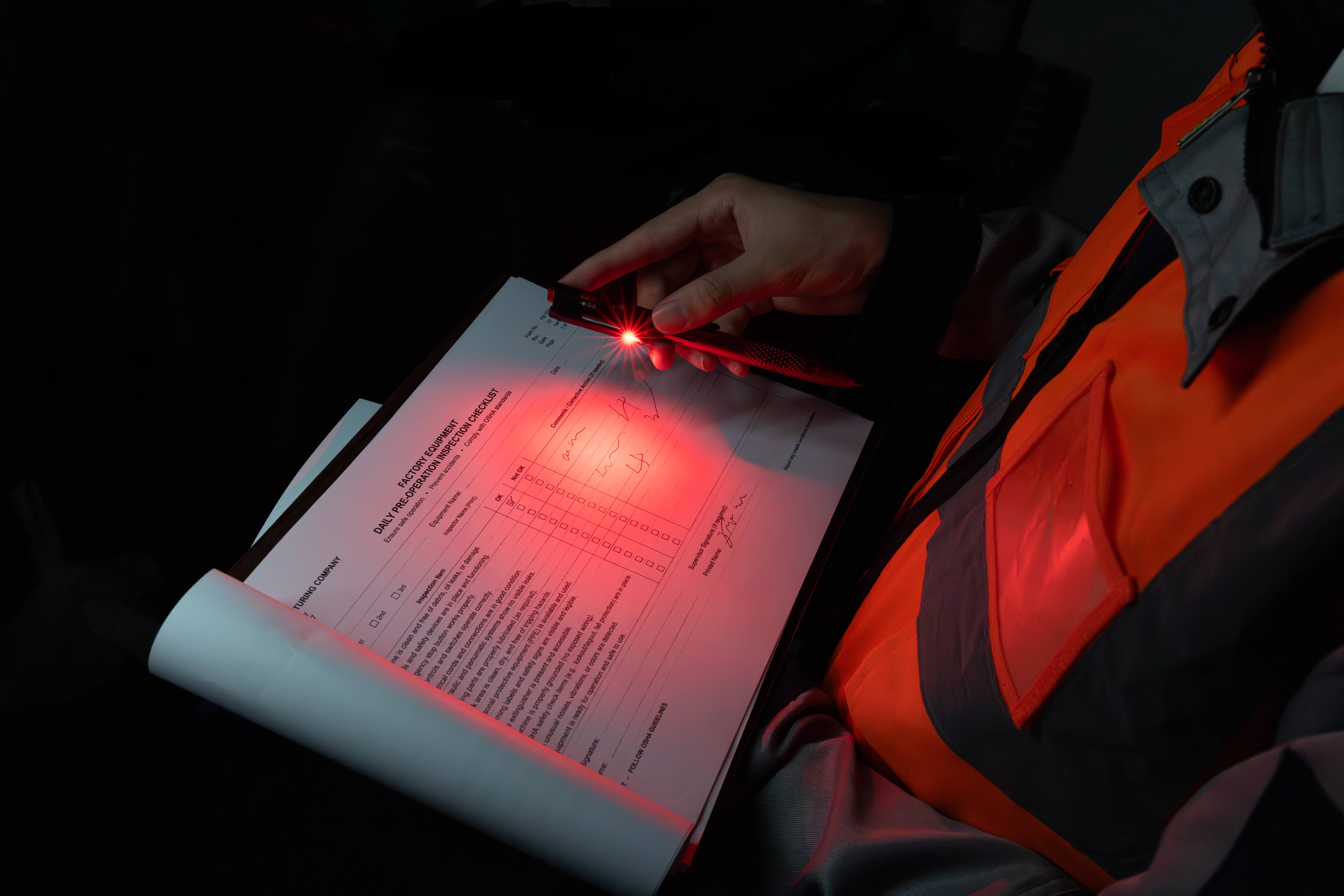 Inspecteur en gilet orange remplissant une liste de contr&ocirc;le &agrave; l'aide de la lampe stylo Olight O'Pen 3 dans l'obscurit&eacute;