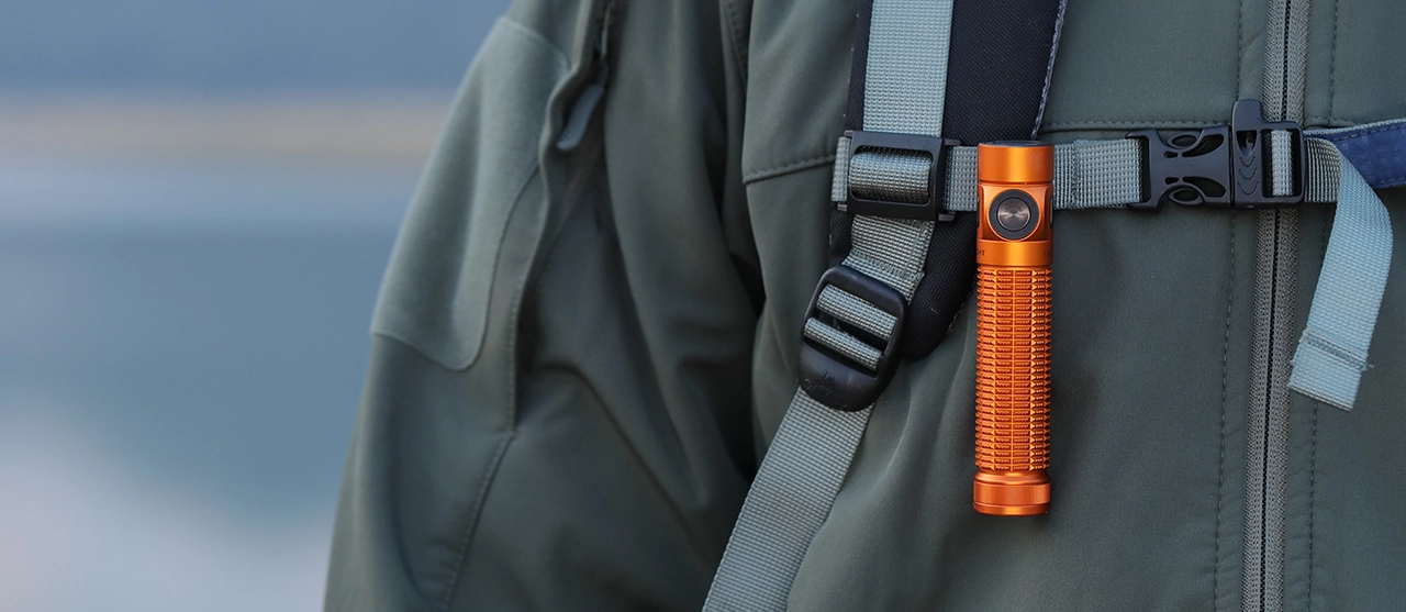 Lampe torche LED orange compacte fix&eacute;e &agrave; la bretelle d'un sac &agrave; dos de randonn&eacute;e.