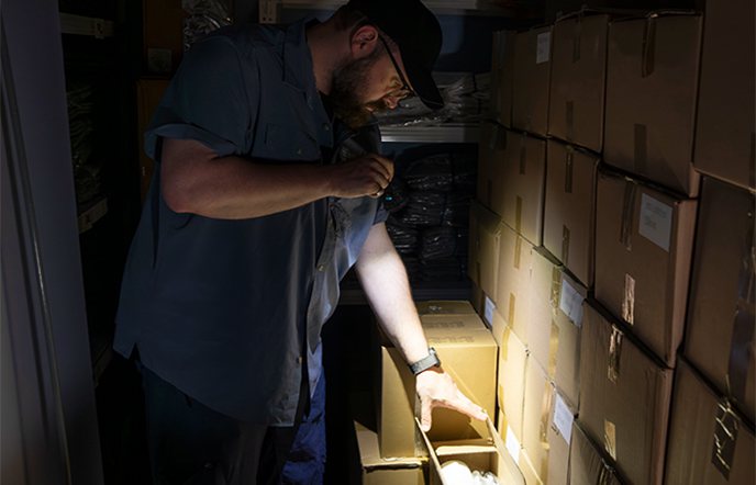 A man in a dark warehouse uses a powerful LED flashlight to inspect inventory on shelves, highlighting the importance of reliable portable lighting.
