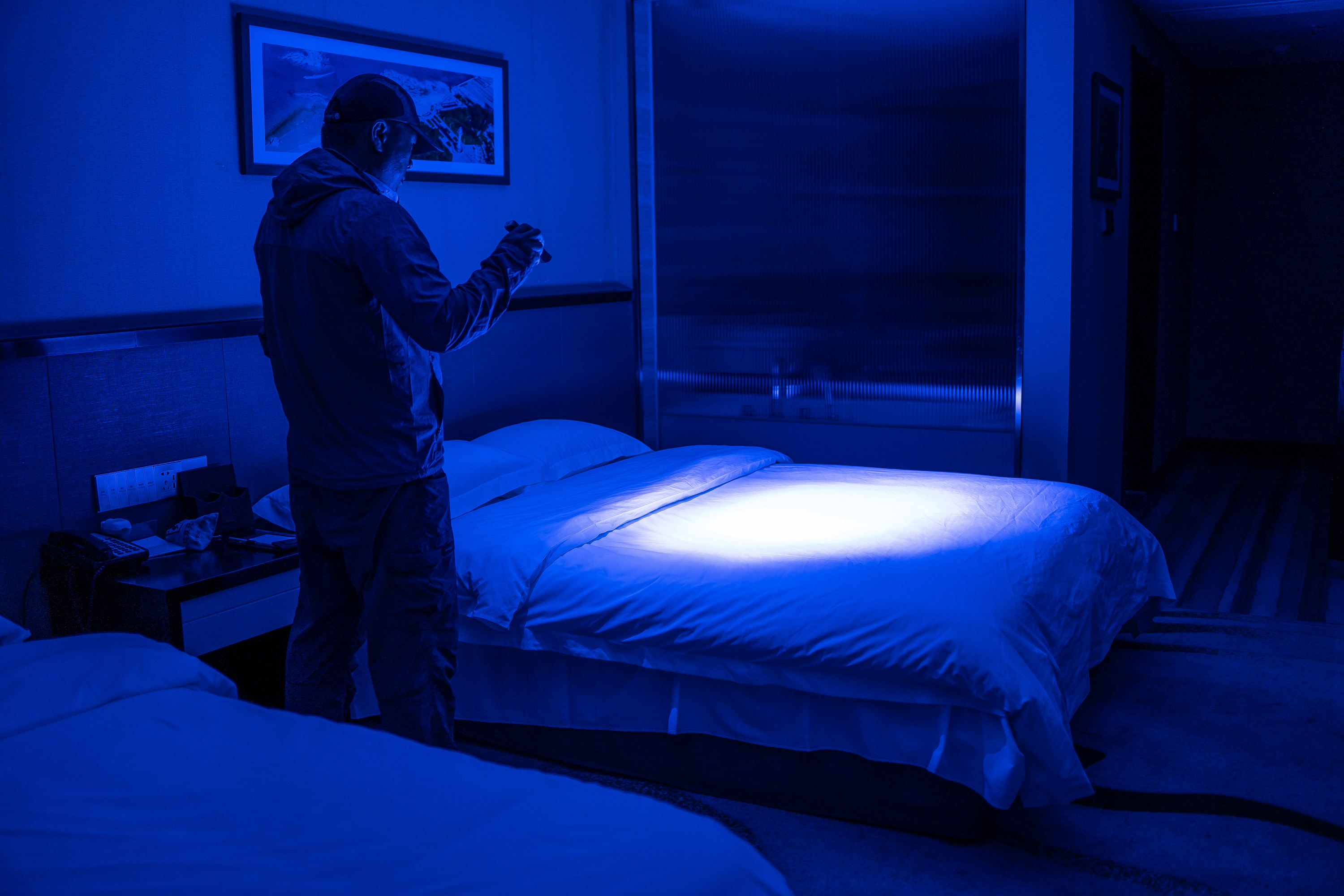 Man using a UV blacklight to inspect hotel bed sheets