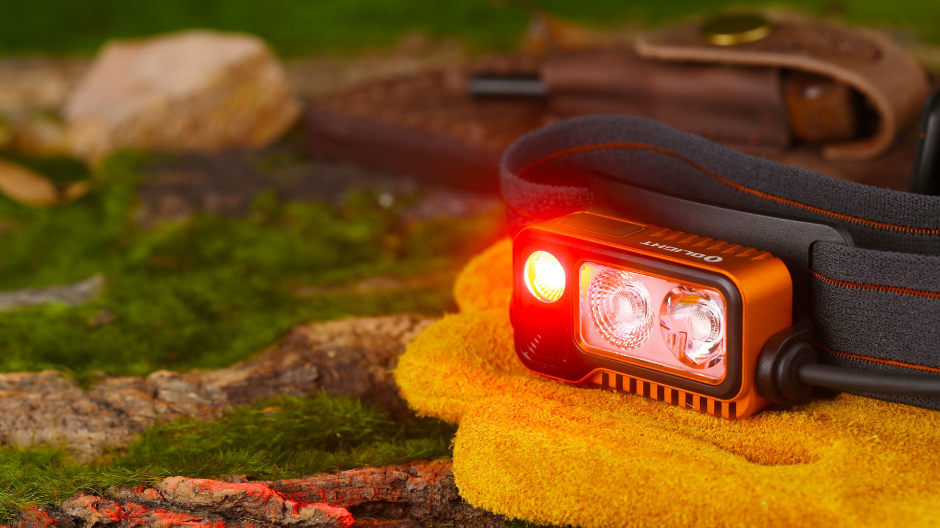 Lampe frontale Olight de couleur orange avec lumi&egrave;re rouge allum&eacute;e.