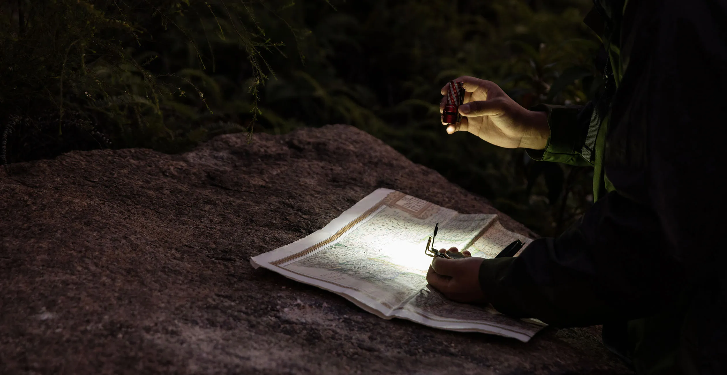 Randonneur &eacute;clairant une carte et une boussole avec une mini lampe torche LED puissante pour s'orienter la nuit en for&ecirc;t.