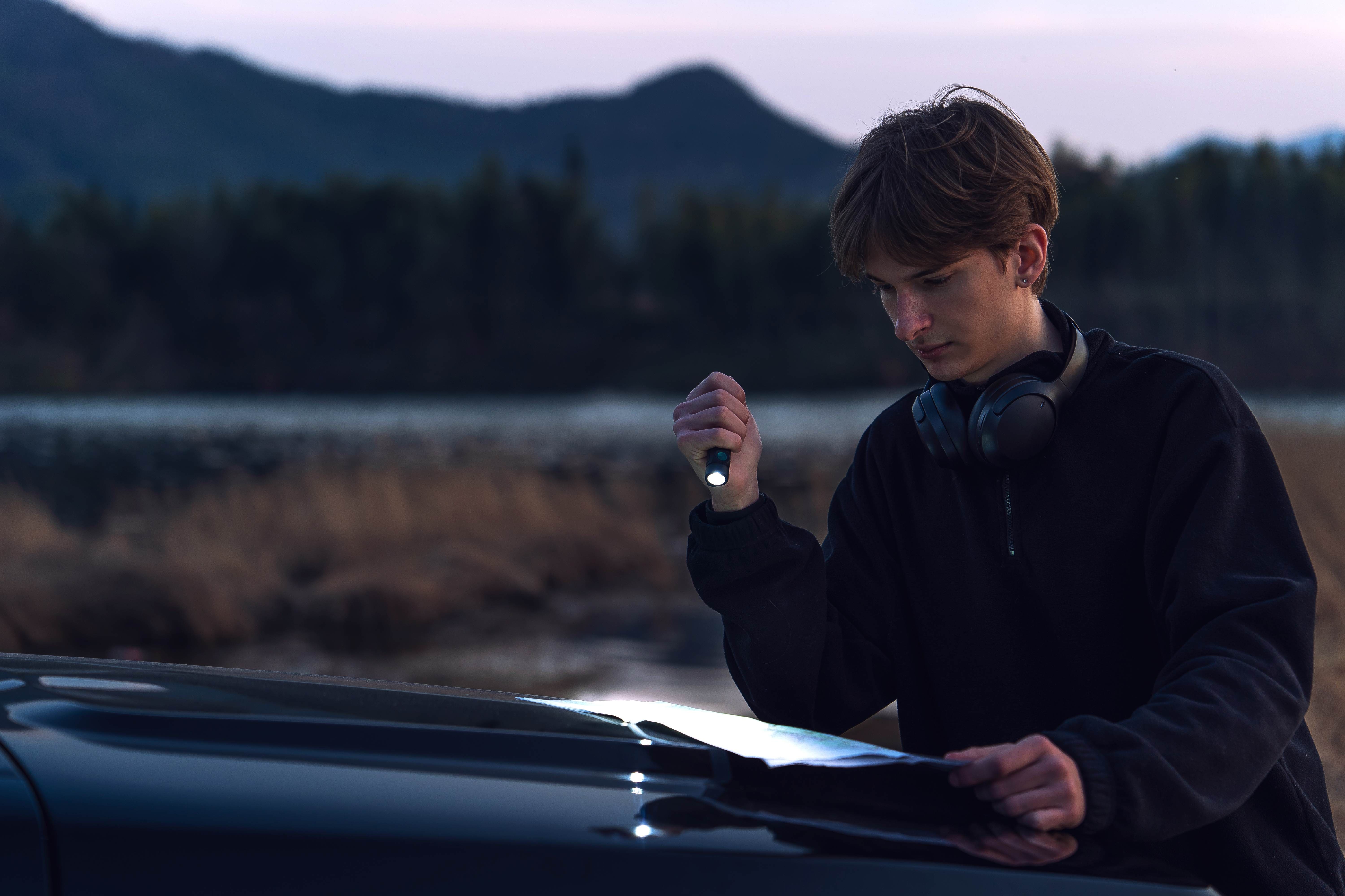 Aventurero utilizando la linterna Olight Baton 4 Pro para leer un mapa en la monta&ntilde;a, cuerpo OAL resistente a ara&ntilde;azos.